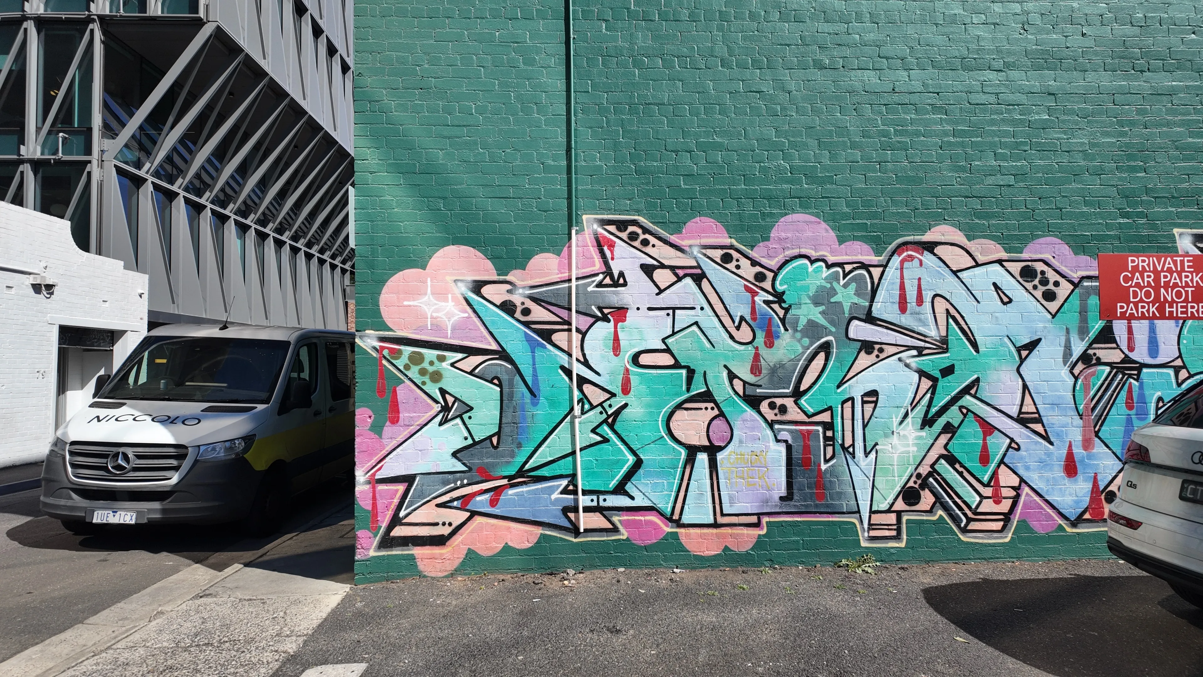 Colourful graffiti on a green brick wall in a laneway beside a parked van.