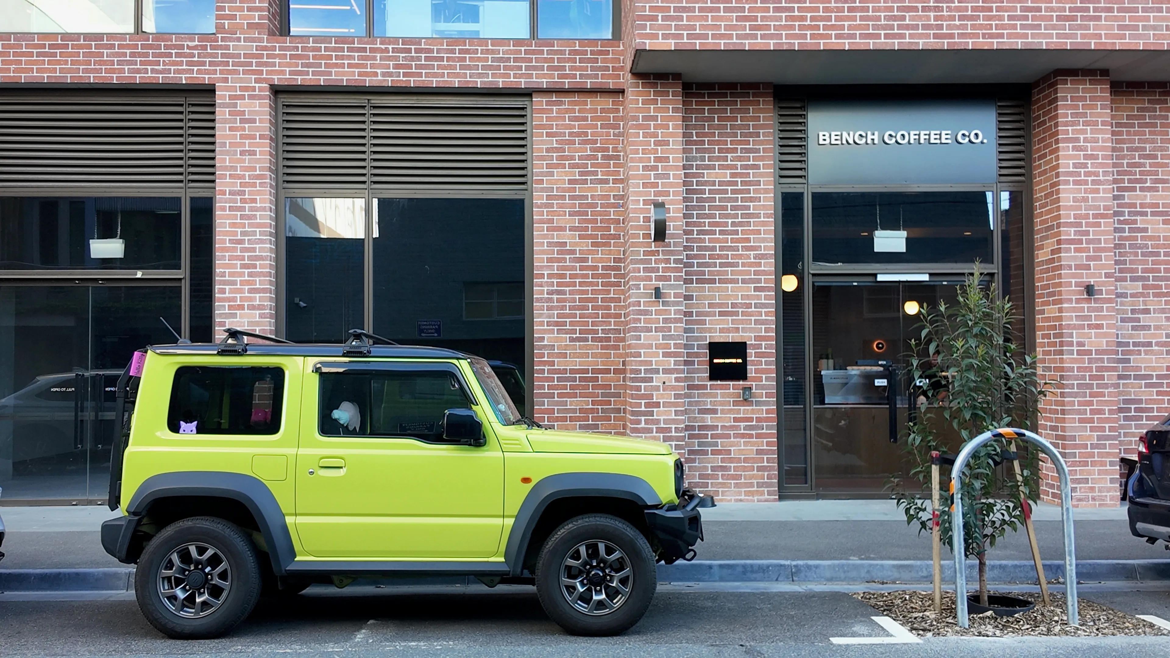 A lime green four-wheel drive parked outside Bench Coffee Co. in a red brick building.