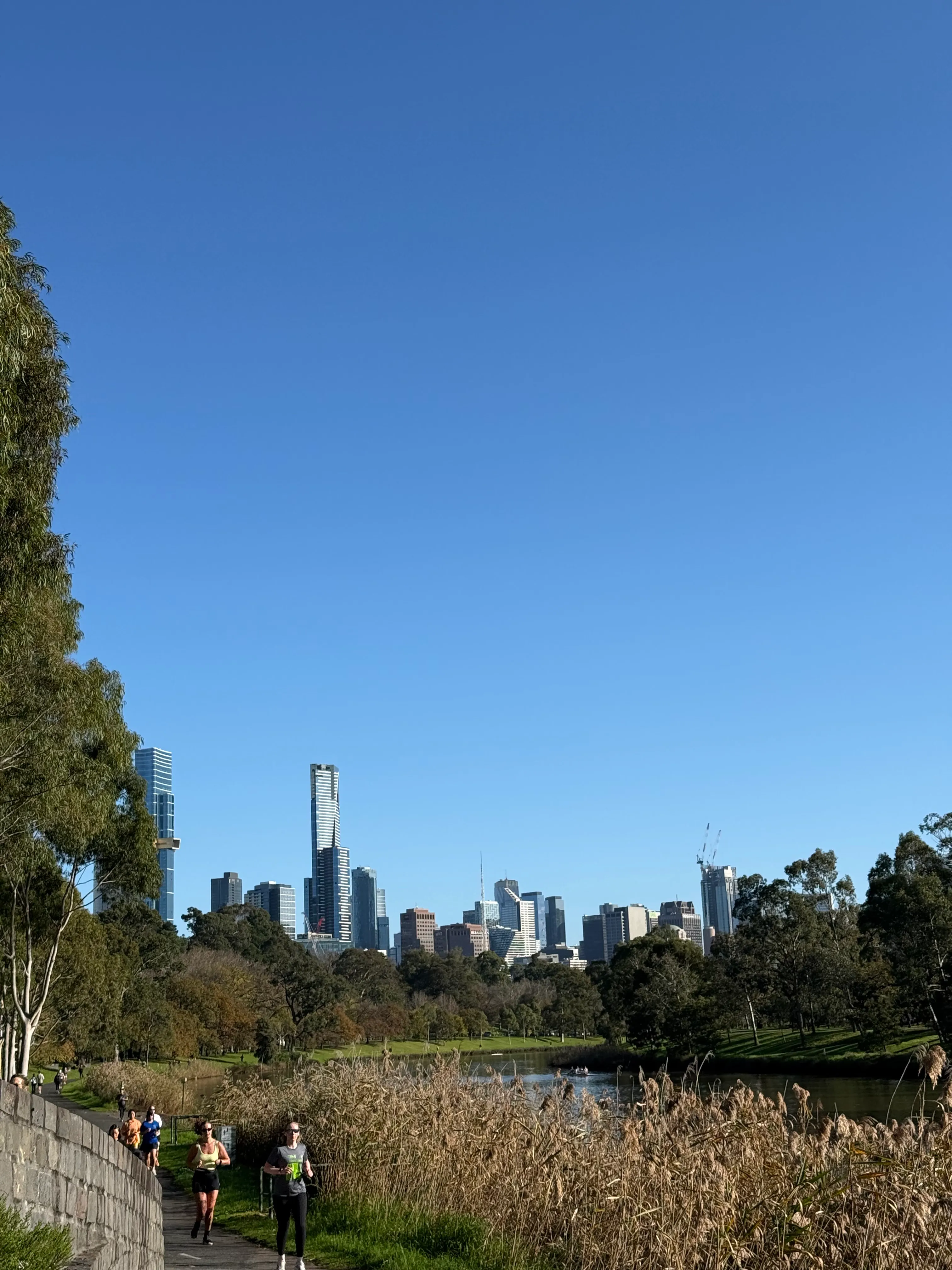 Melbourne skyline above the Yarra with walkers on the riverside path.