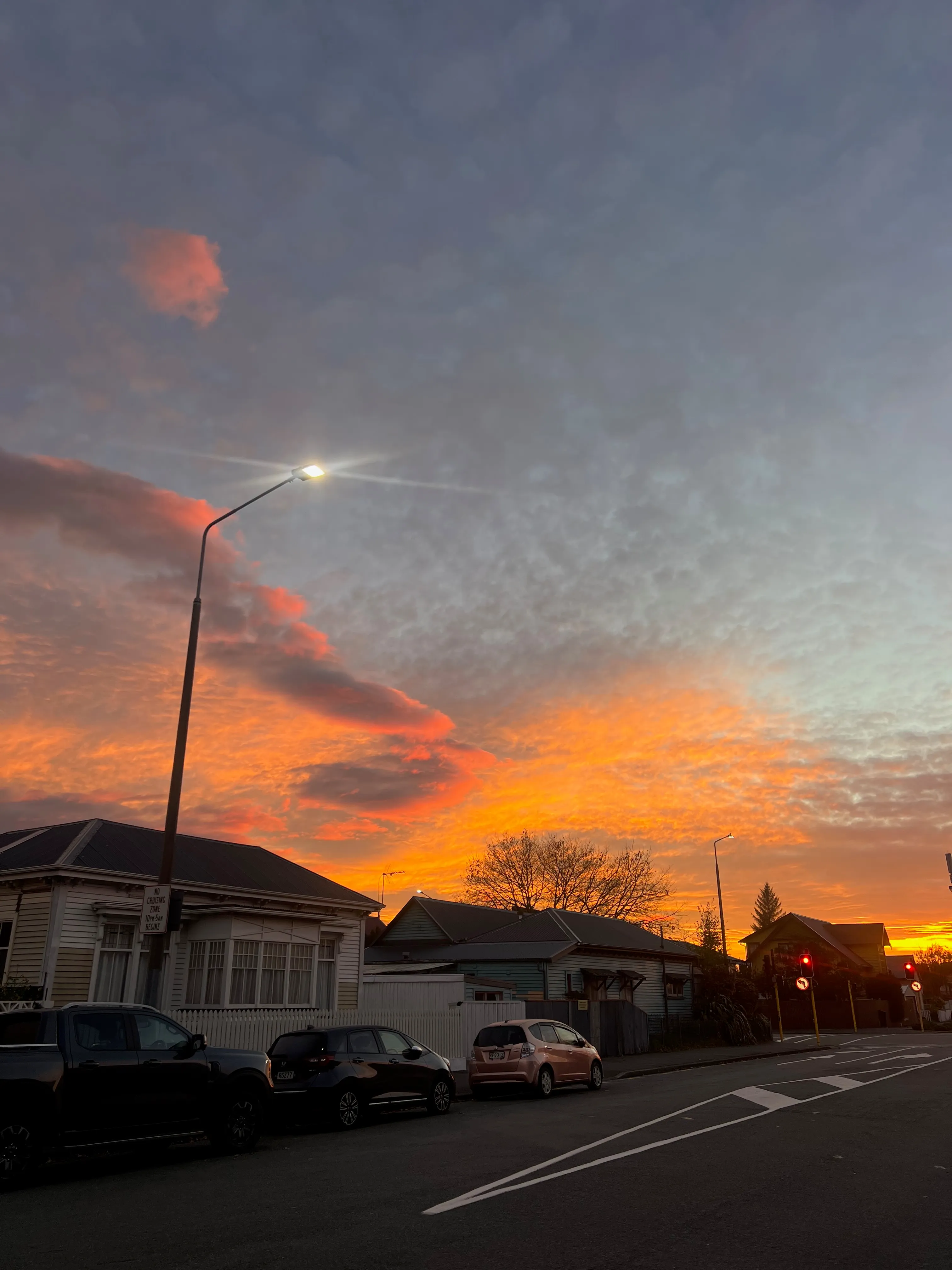 An orange sunrise glowing over a quiet street of villas and parked cars.