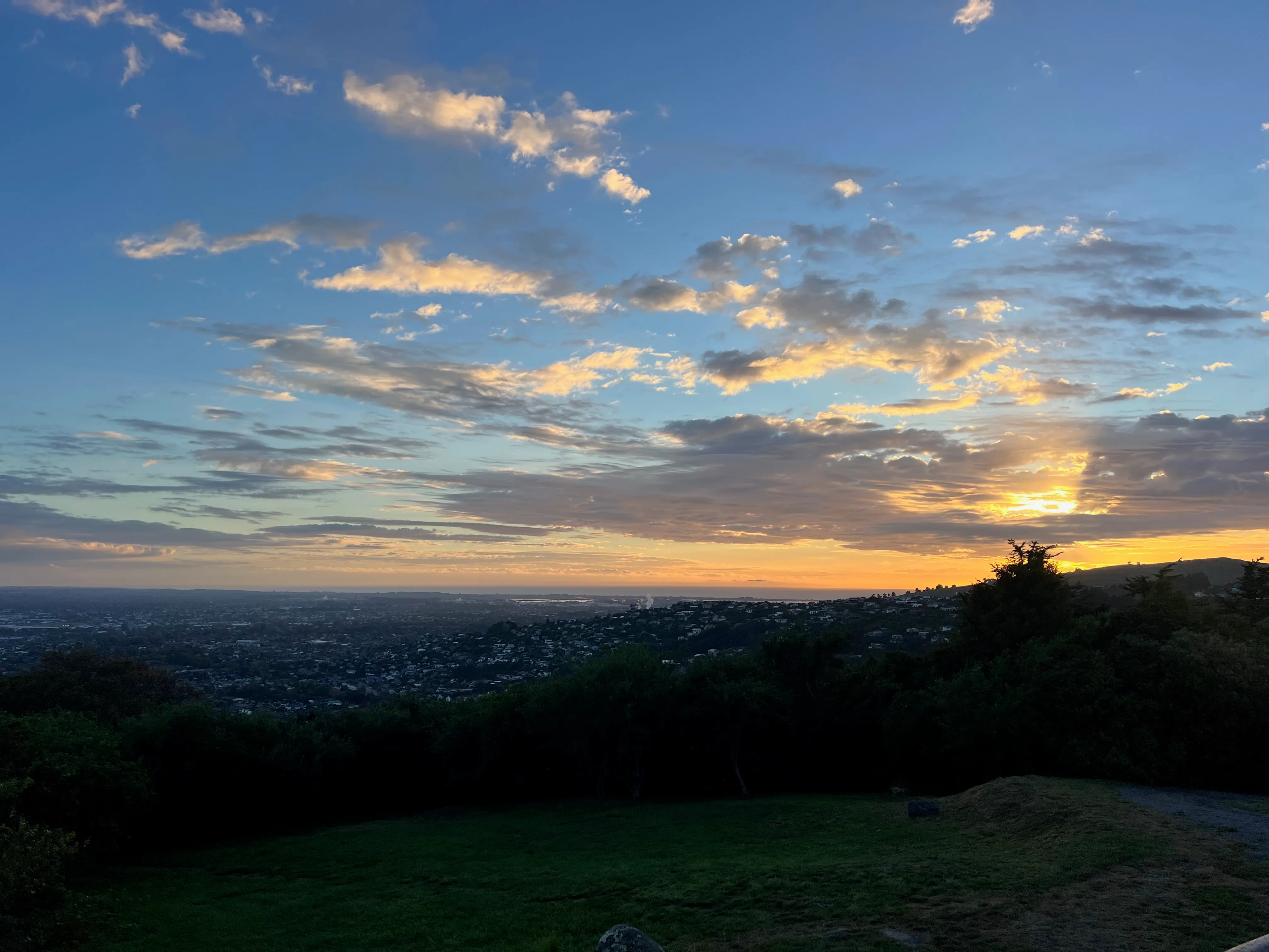 The sun rising over Christchurch, seen from a grassy hillside.