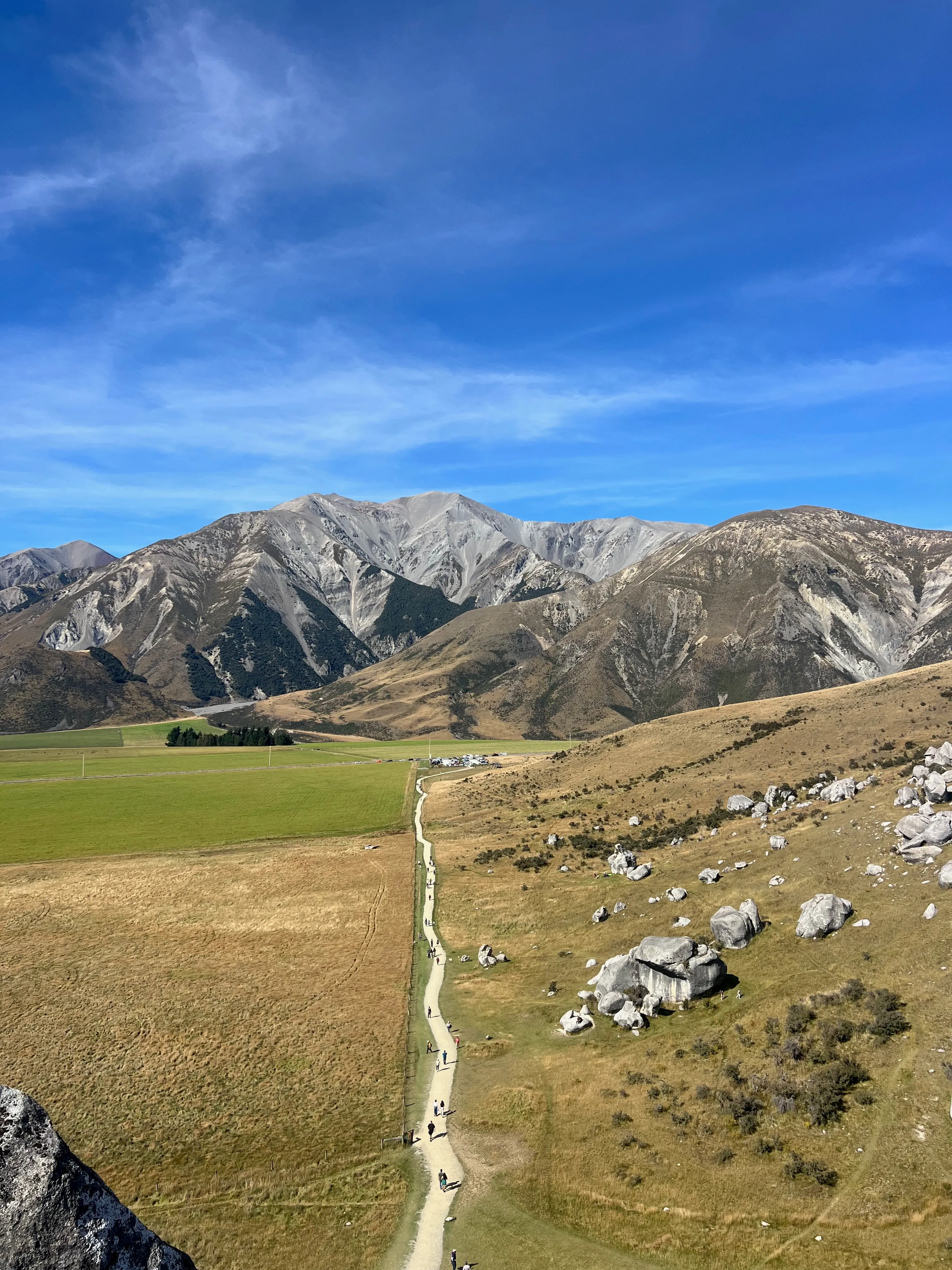 A path winding through a boulder-strewn valley below bare grey mountains.