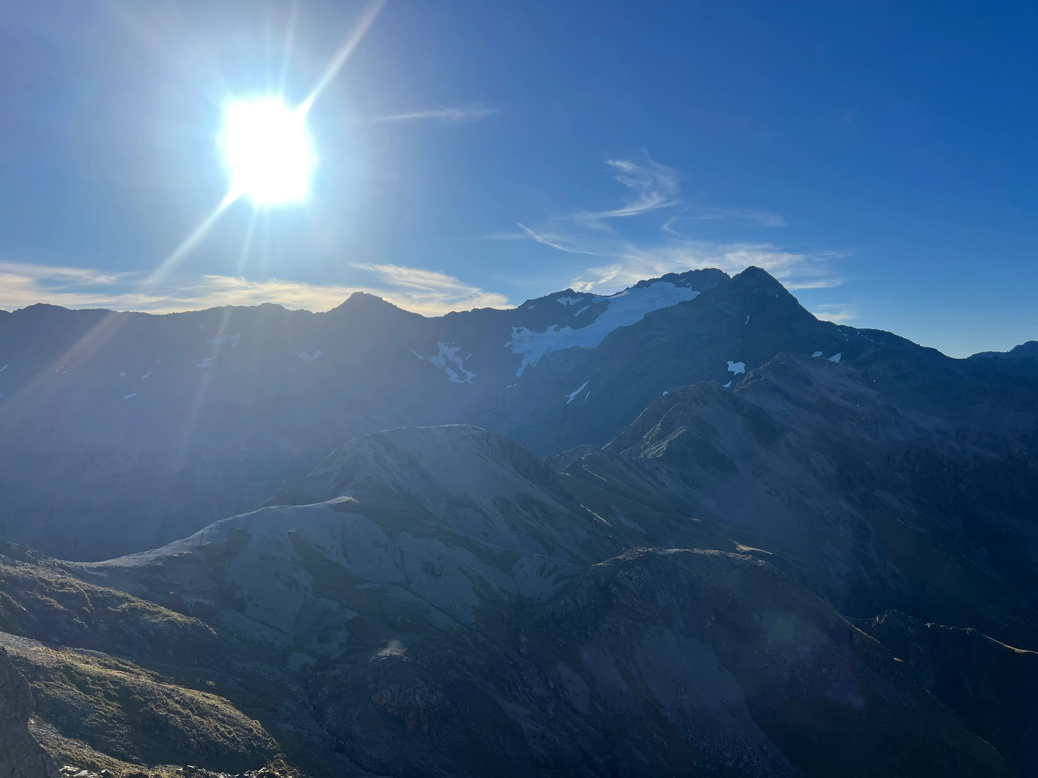 The sun shining over a mountain with patches of snow.