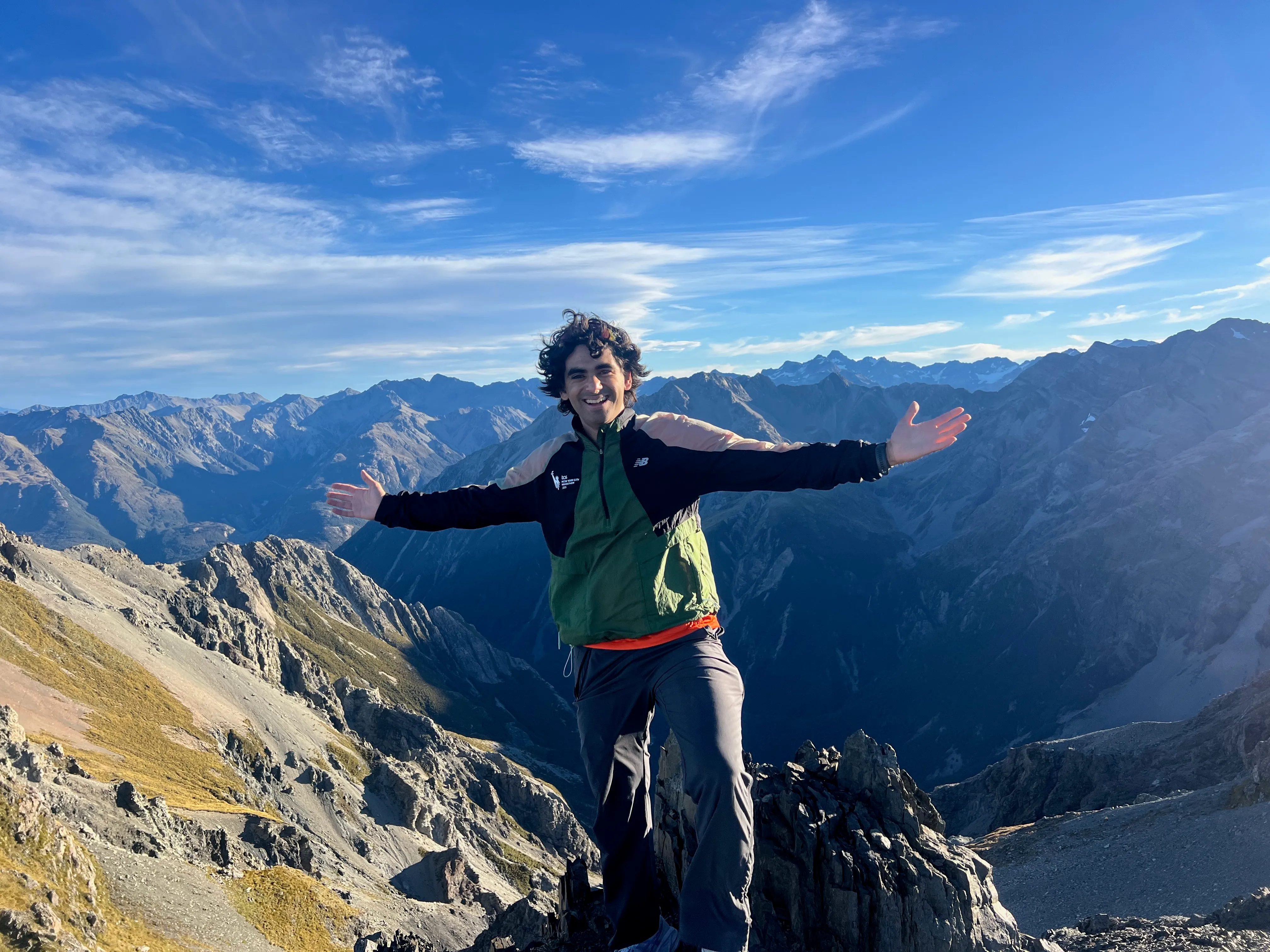 A hiker with arms spread wide on the summit, above a deep valley.