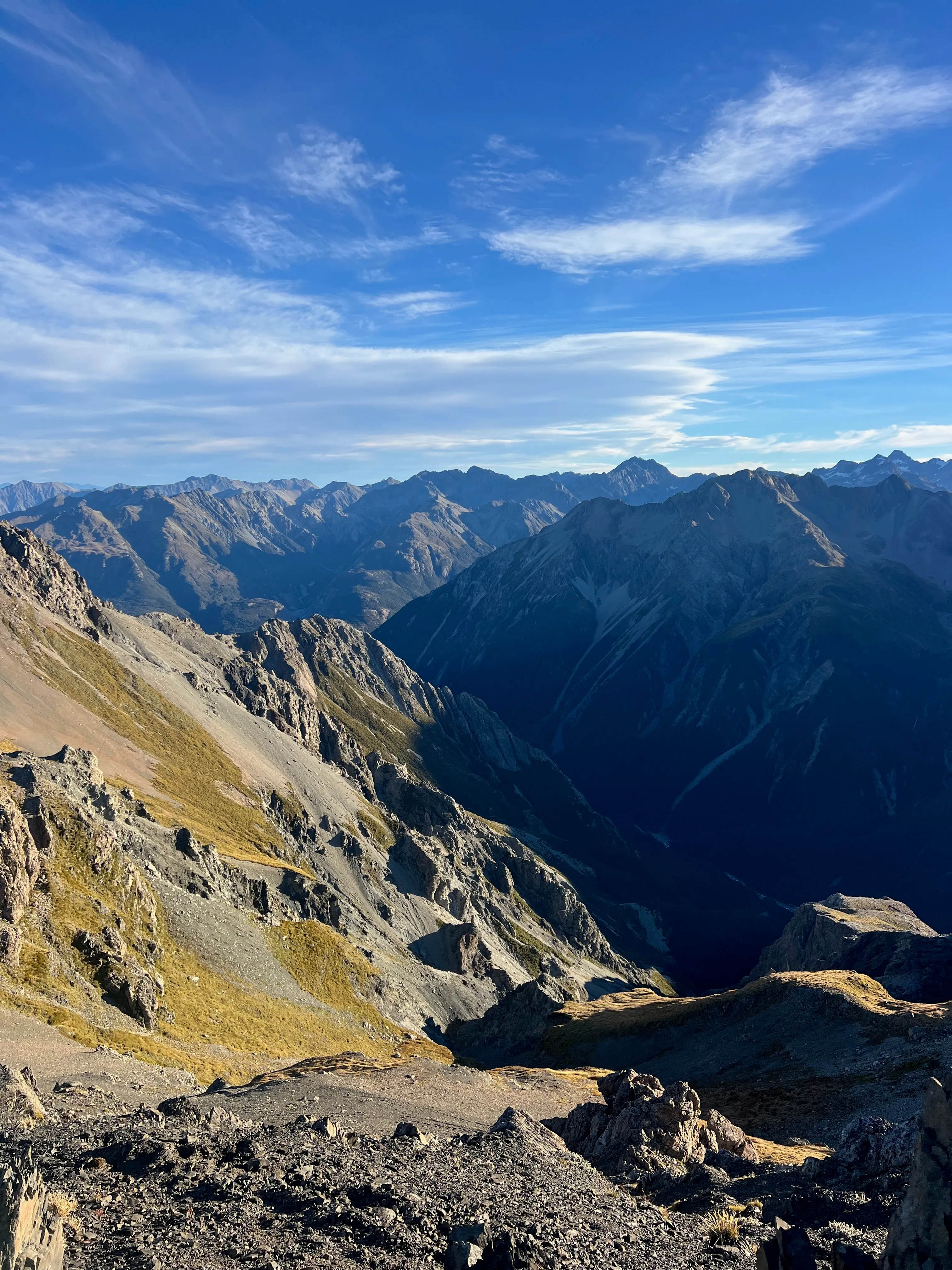 Looking down from the summit into a shadowed valley ringed by peaks.