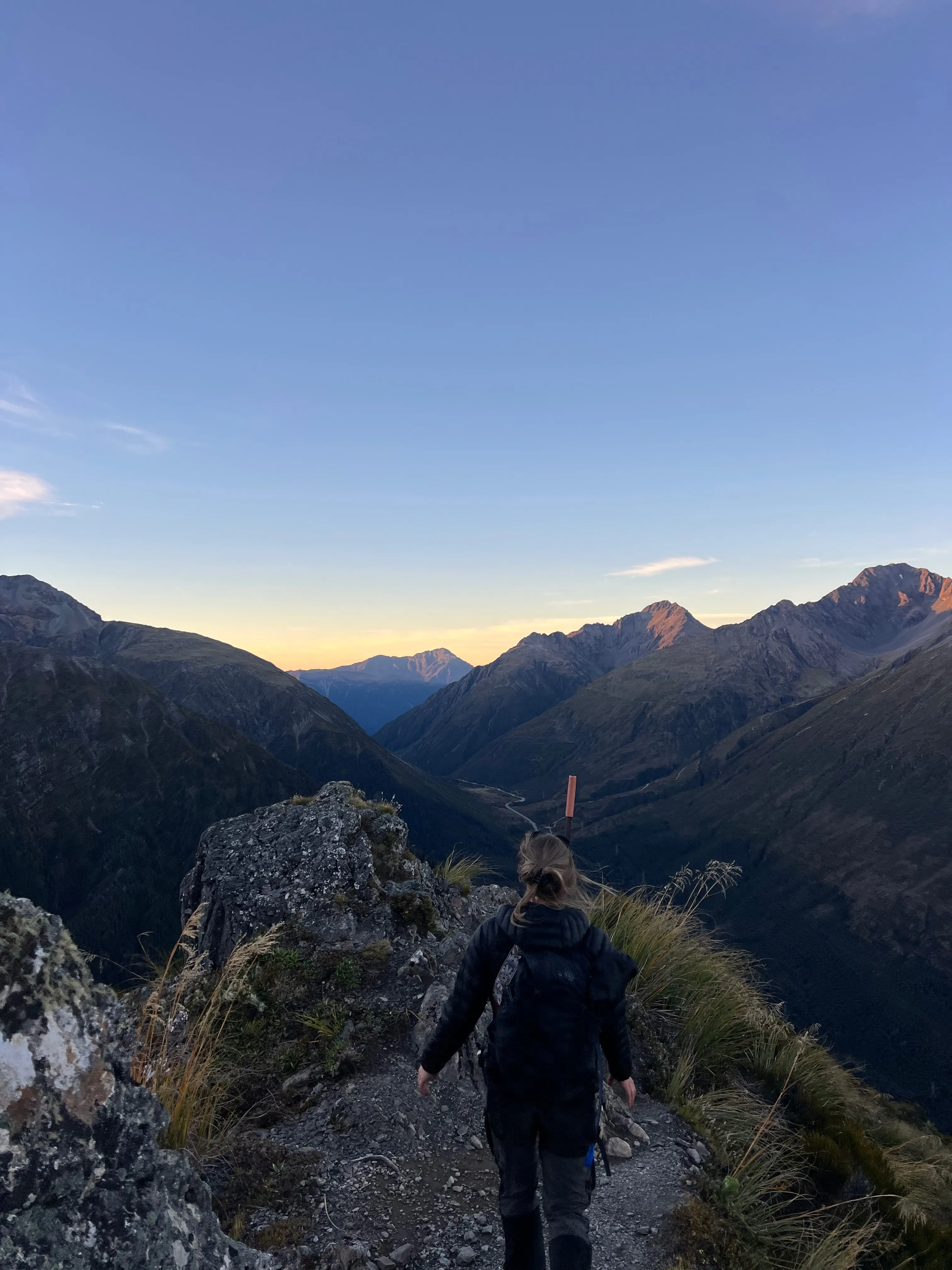 A hiker heading down a narrow track at dusk between dark mountains.
