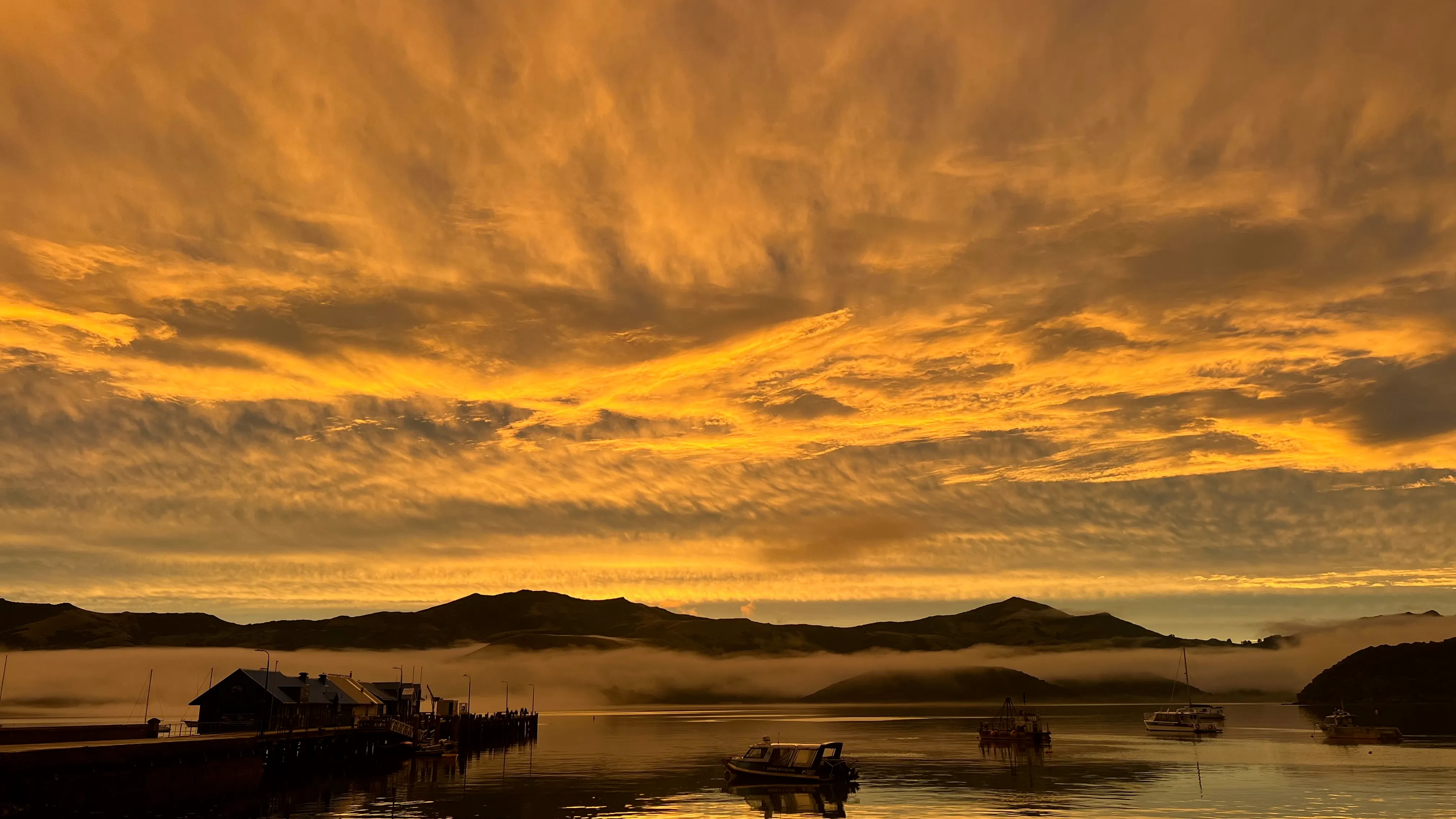 Streaks of orange cloud above the dark hills and a wharf on the harbour.