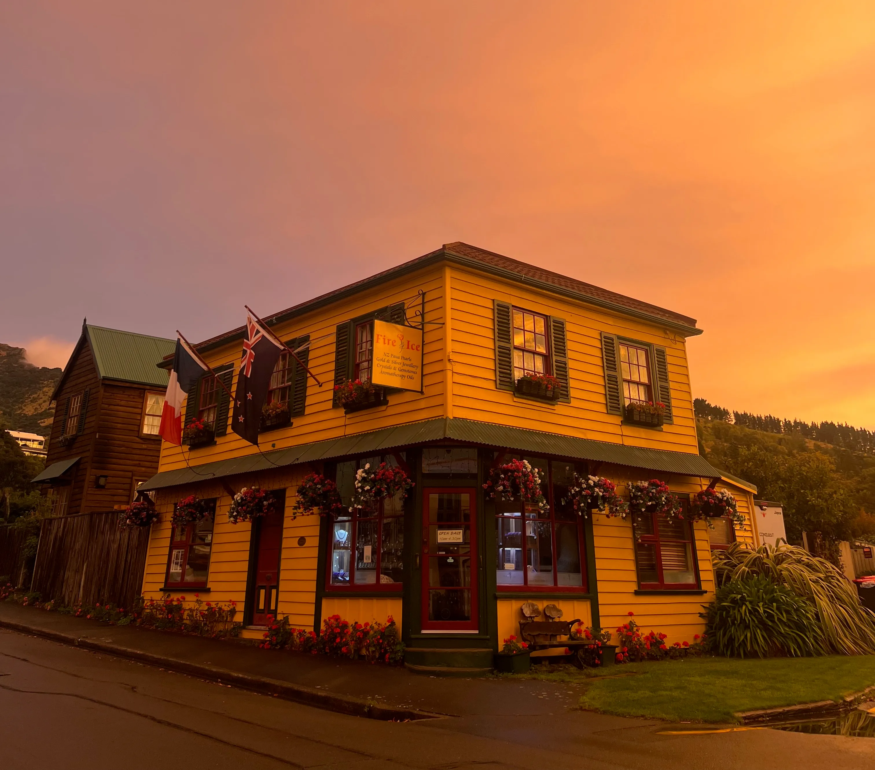 A yellow two-storey wooden building with French and New Zealand flags and hanging flower baskets.