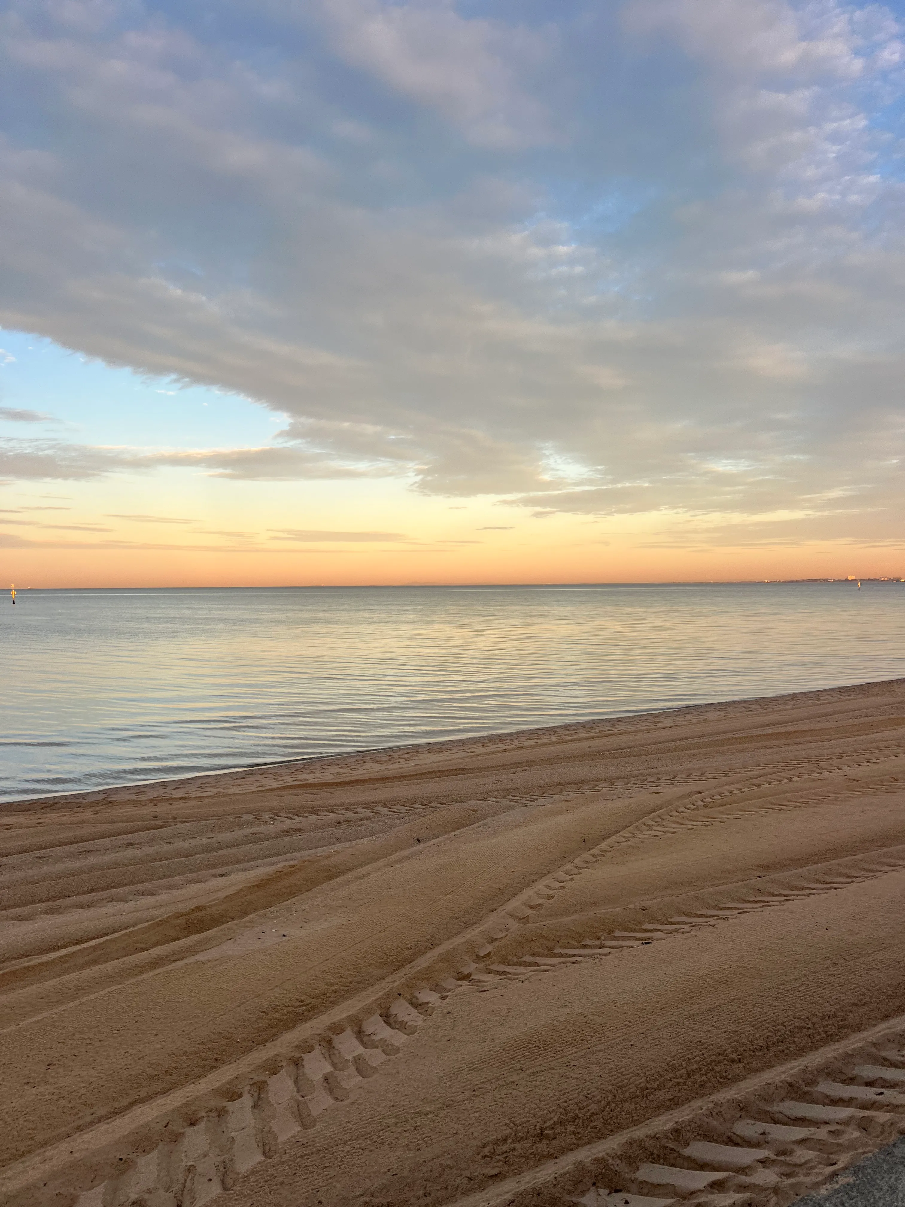 Sunrise over the bay above tyre-marked sand.