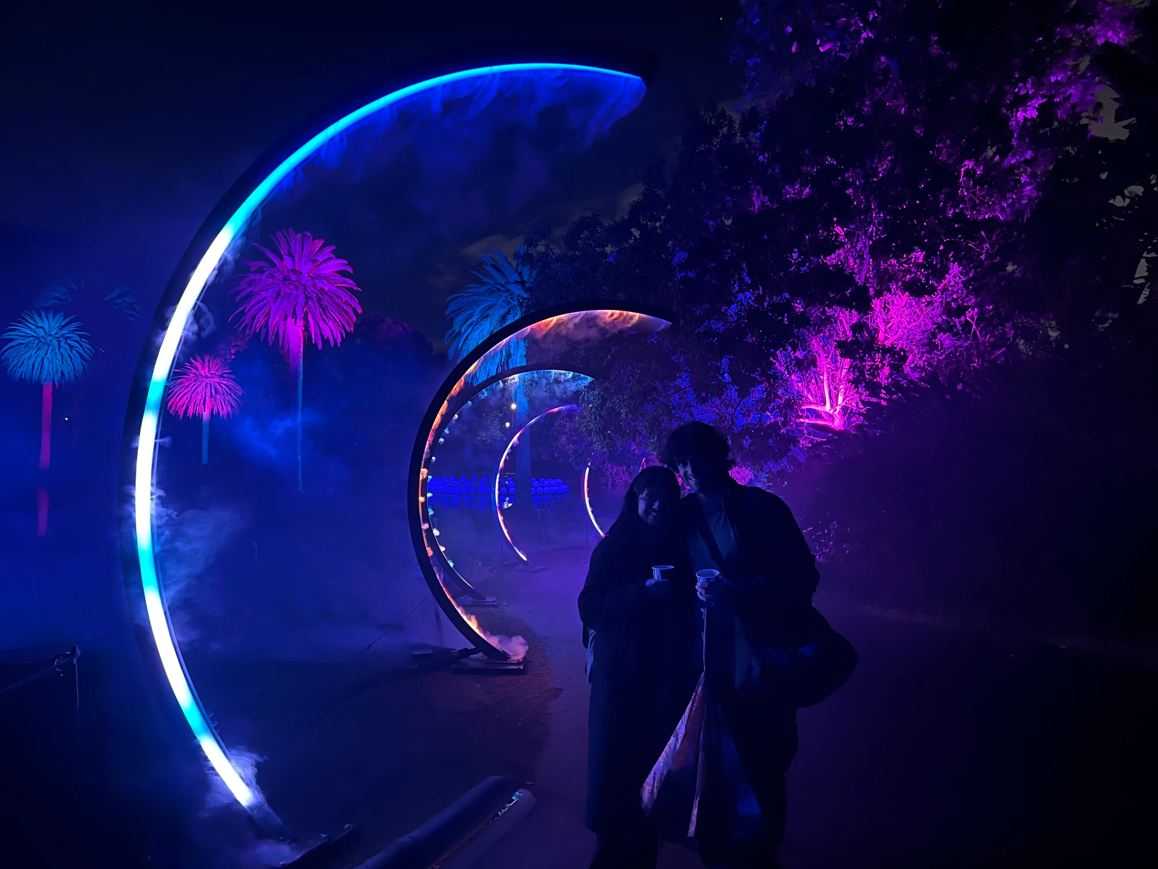 Two people walking through a glowing tunnel of lights at night.