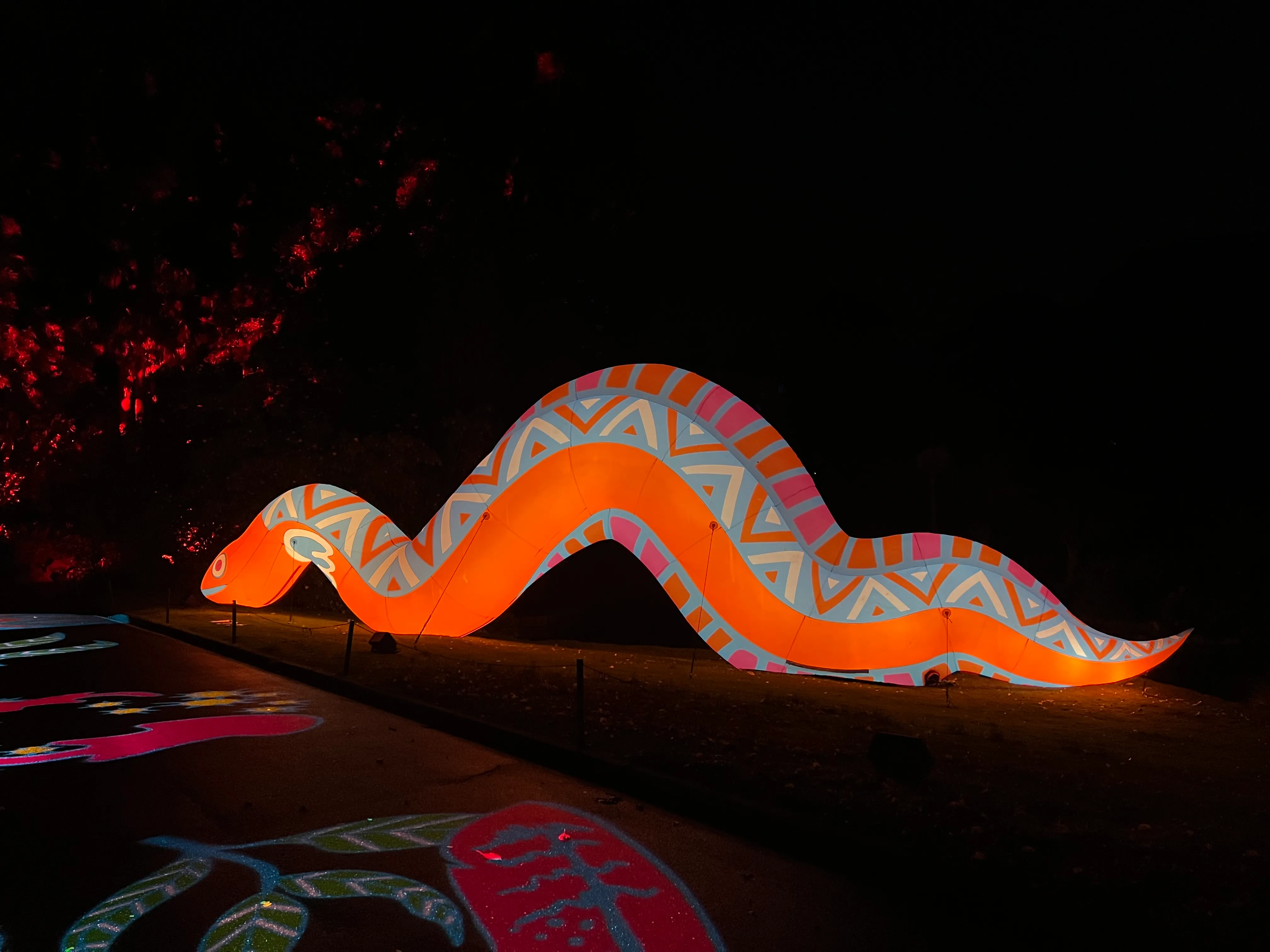 A glowing orange light sculpture winding through the dark gardens.