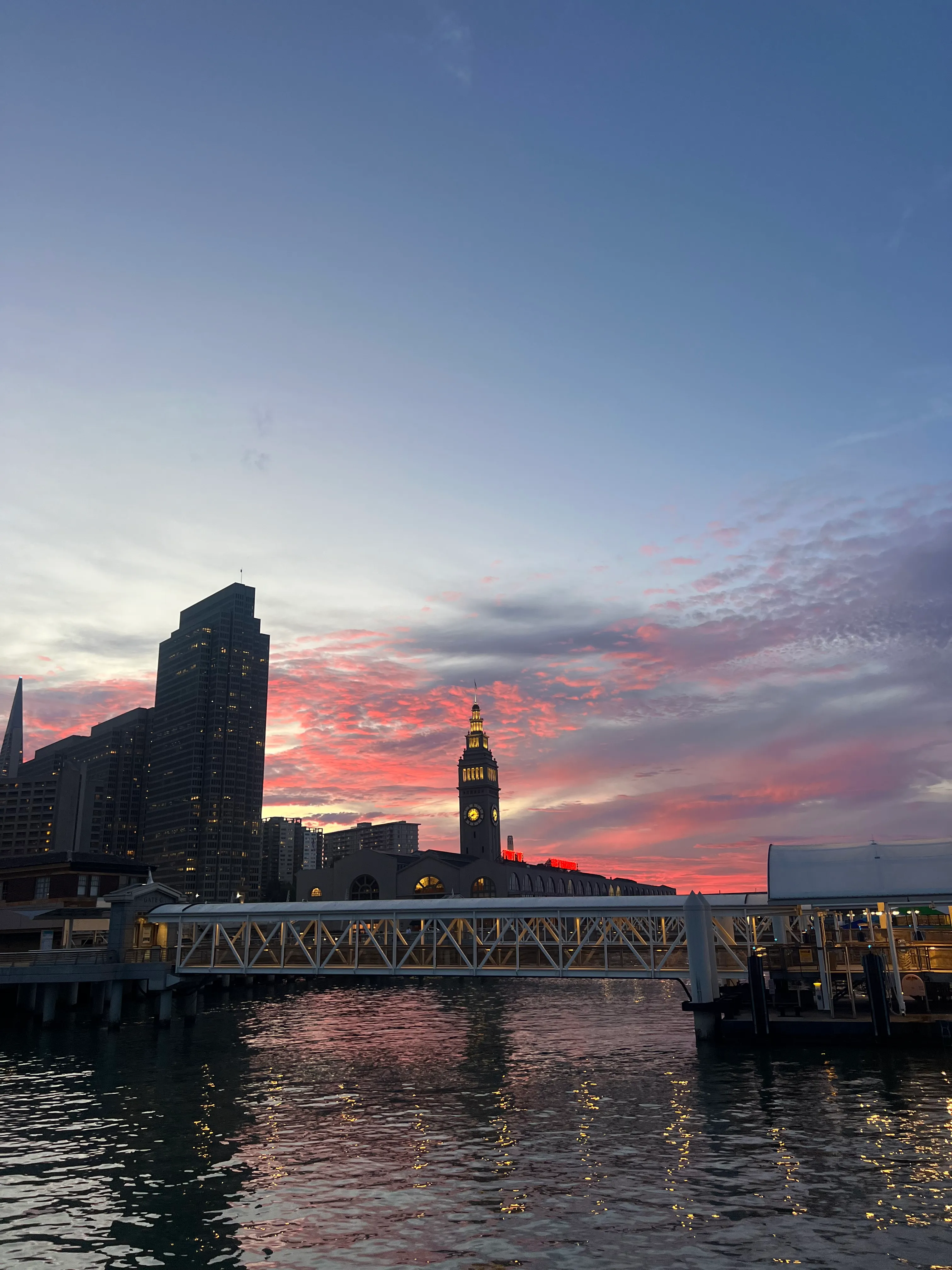 The Ferry Building and its clock tower across the water at sunset.