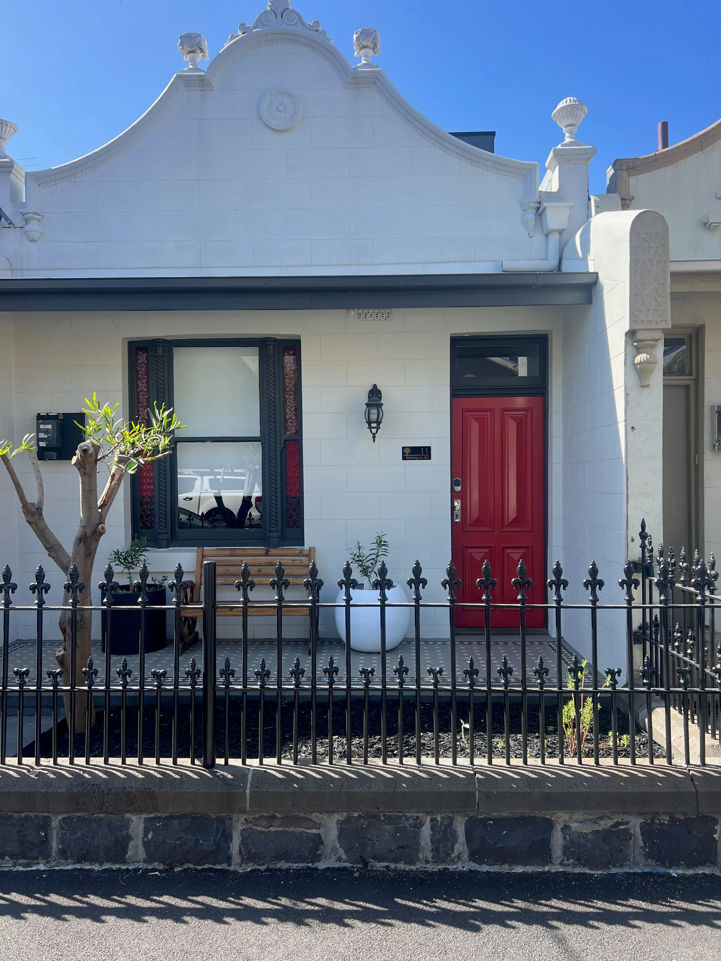 A white terrace house with a red door and an iron fence.