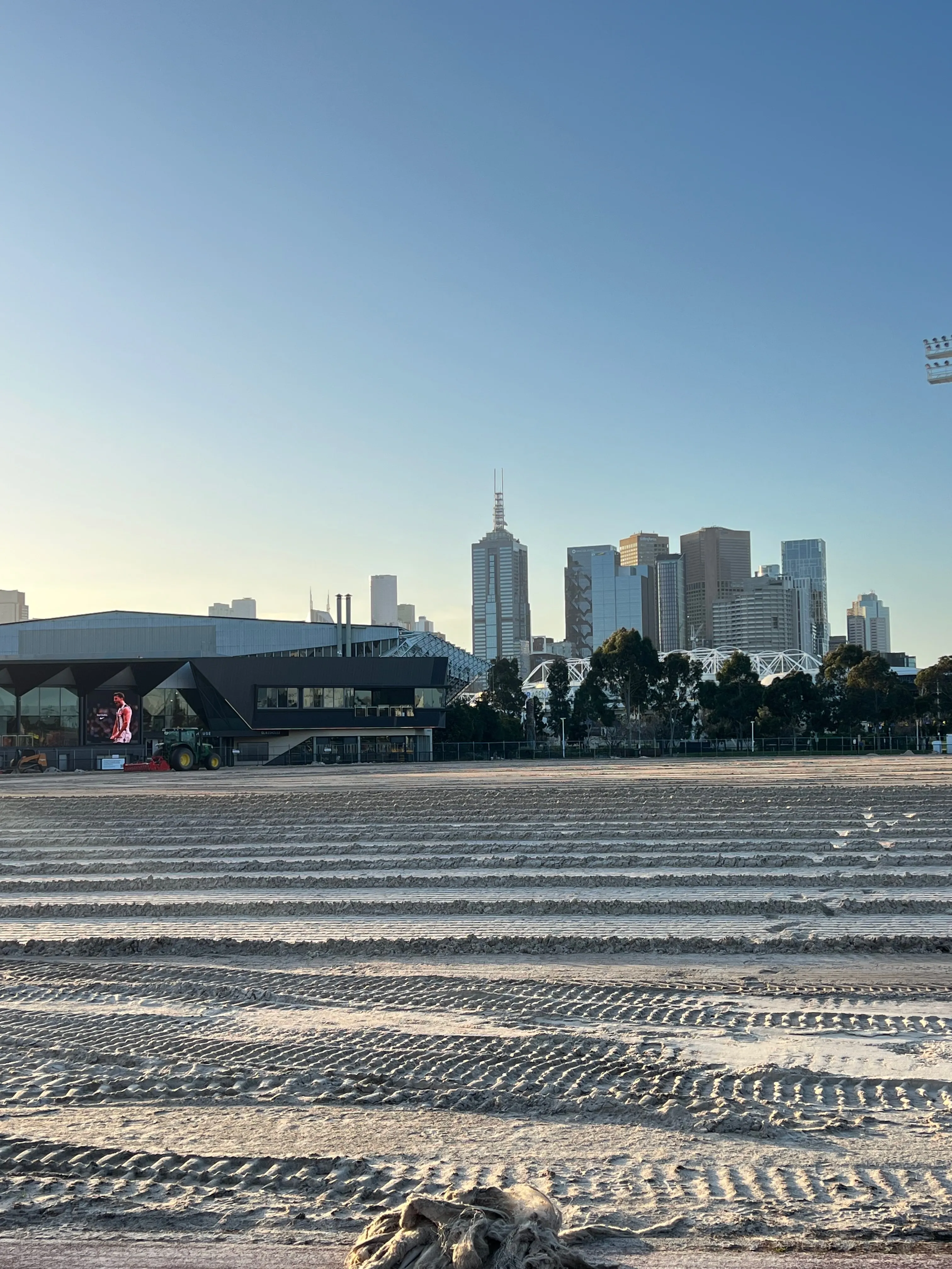 Melbourne skyline beyond sports buildings and a field under construction.