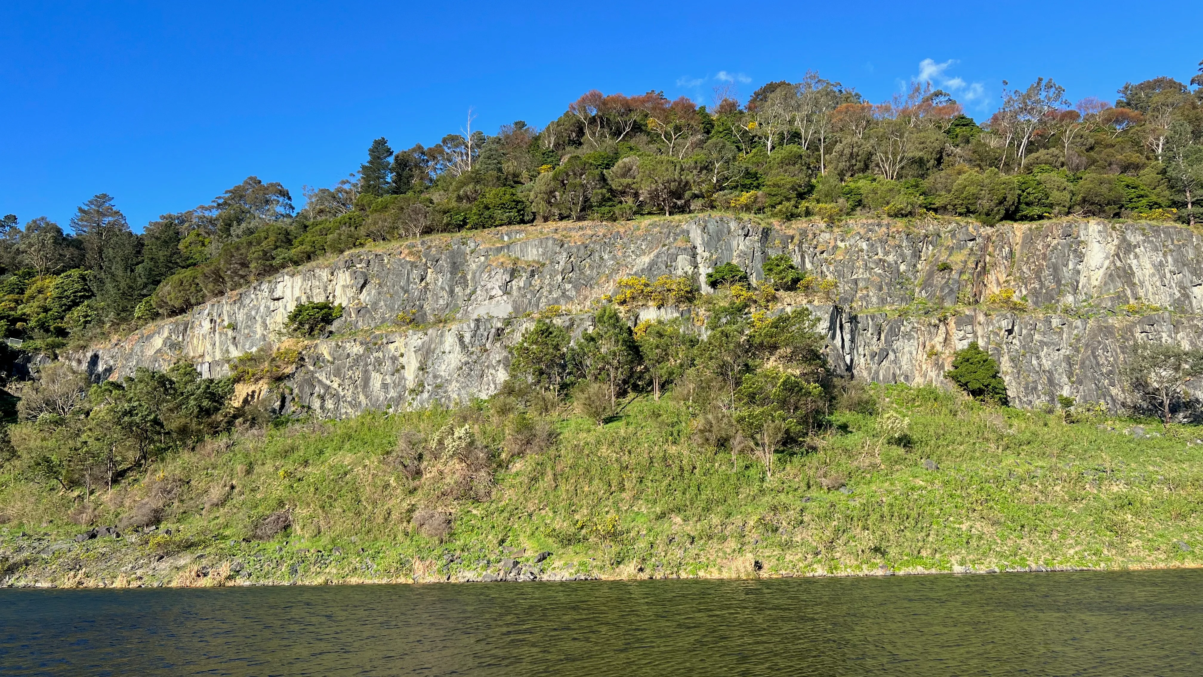 Sunlit rocky cliffs and trees above a lake.