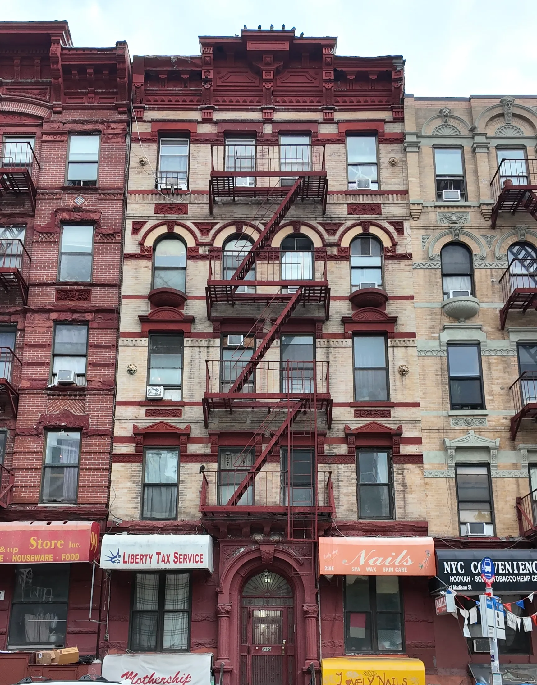 An ornate red and cream brick apartment building with fire escapes and storefronts.