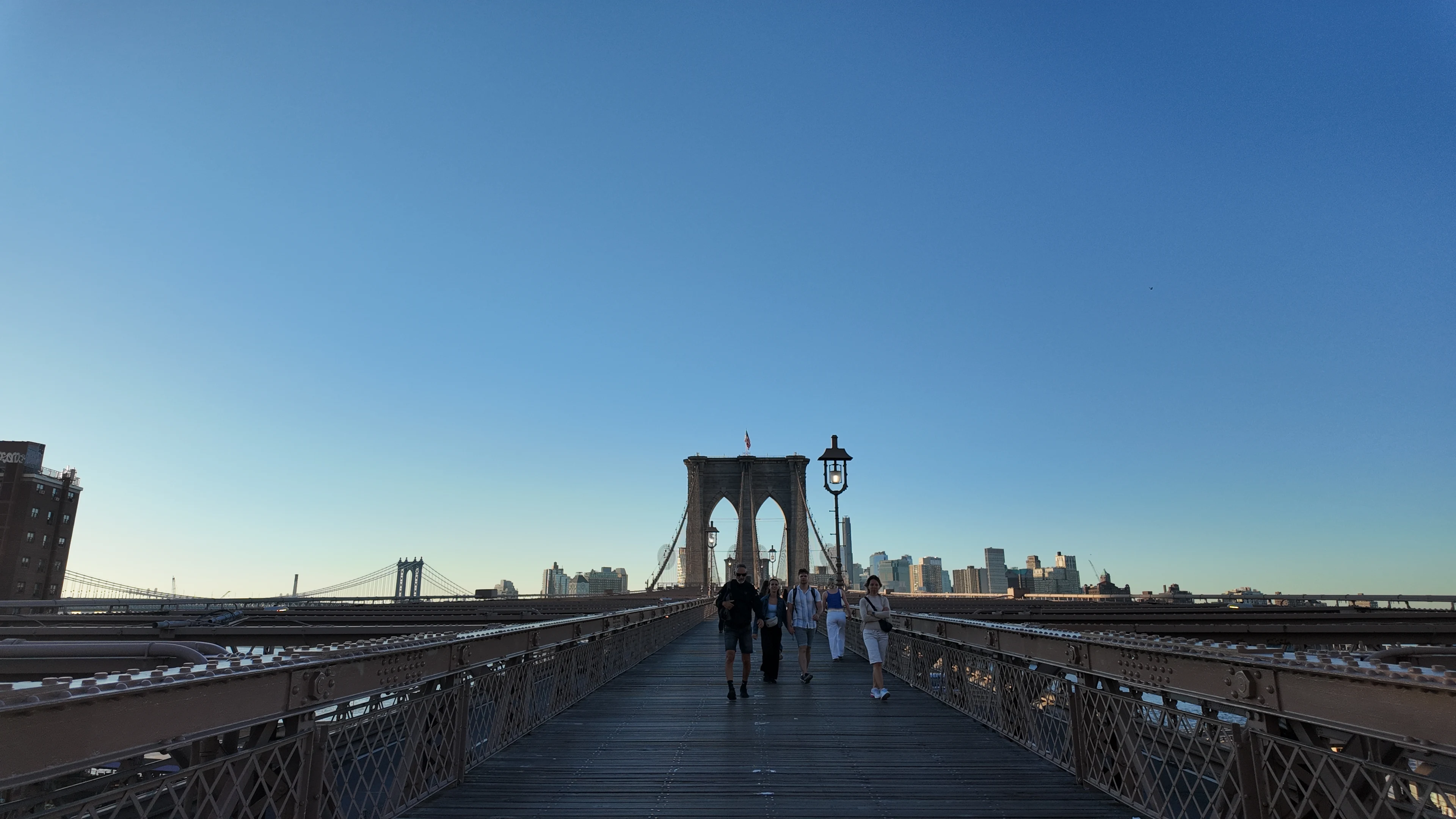 Walkers on the Brooklyn Bridge promenade toward its stone tower.