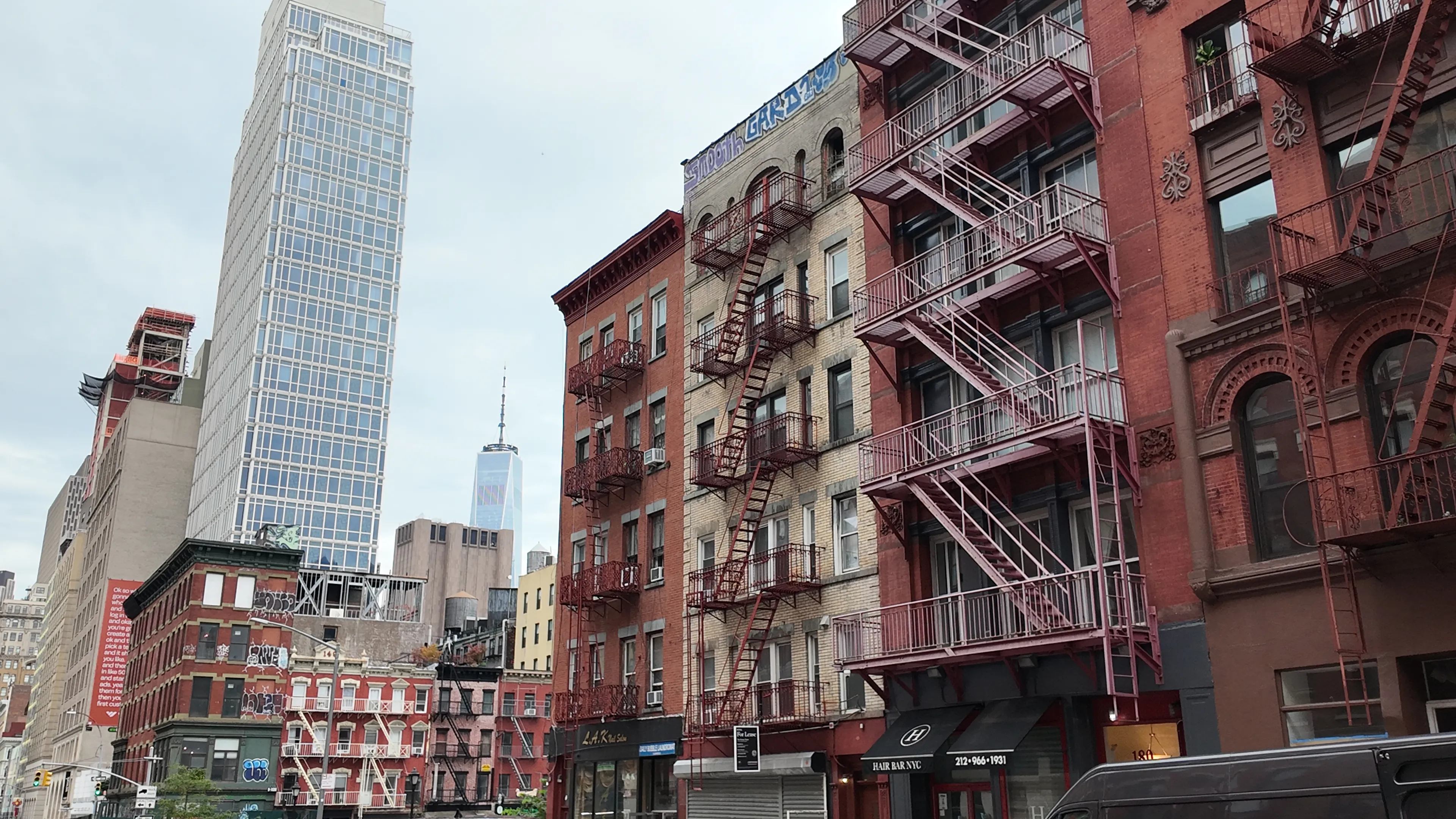 Brick buildings with metal fire escapes beside taller towers on a New York street.