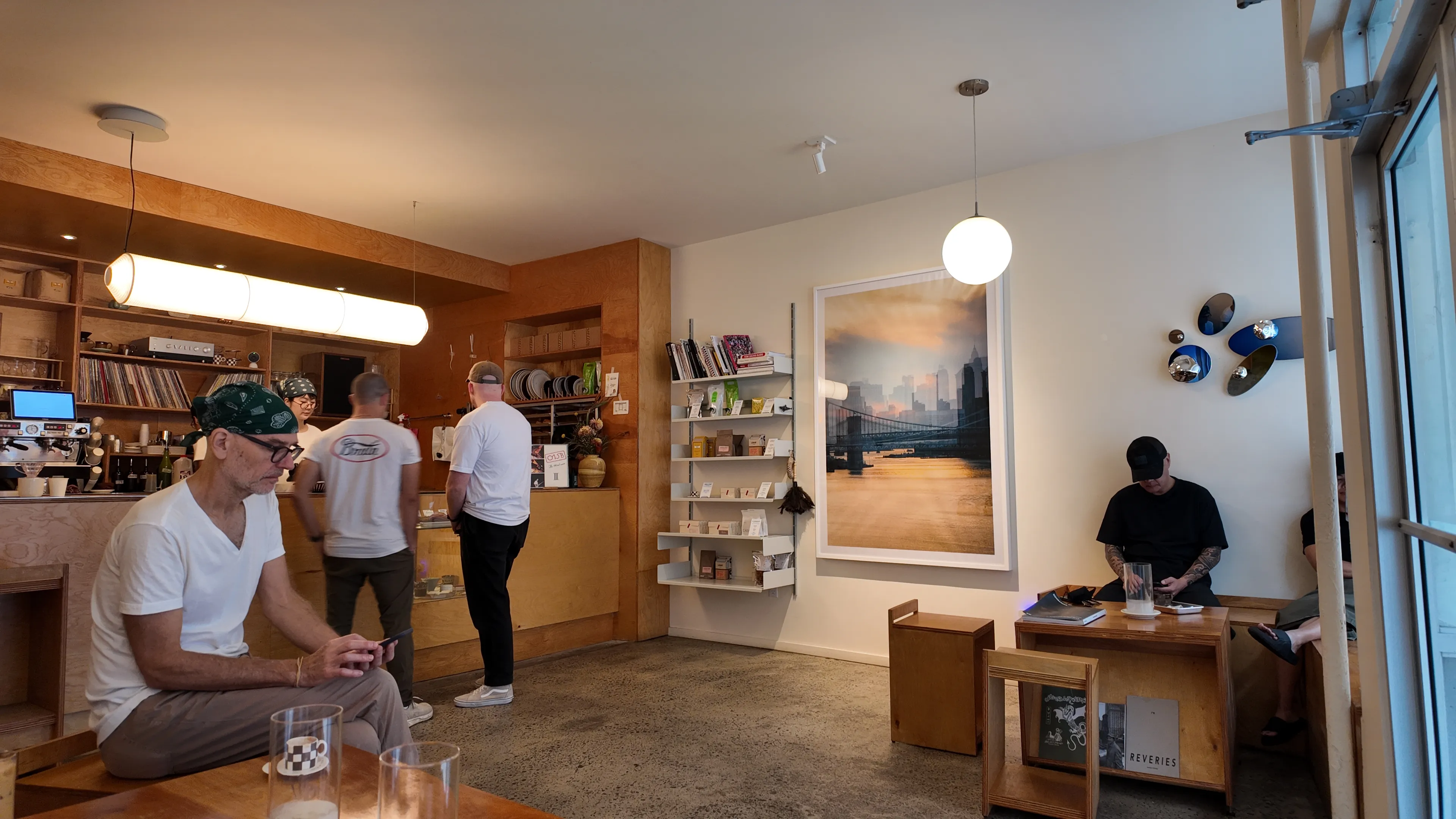 Customers at the counter and seated inside a wood-panelled coffee shop, with a framed skyline photograph on the wall.