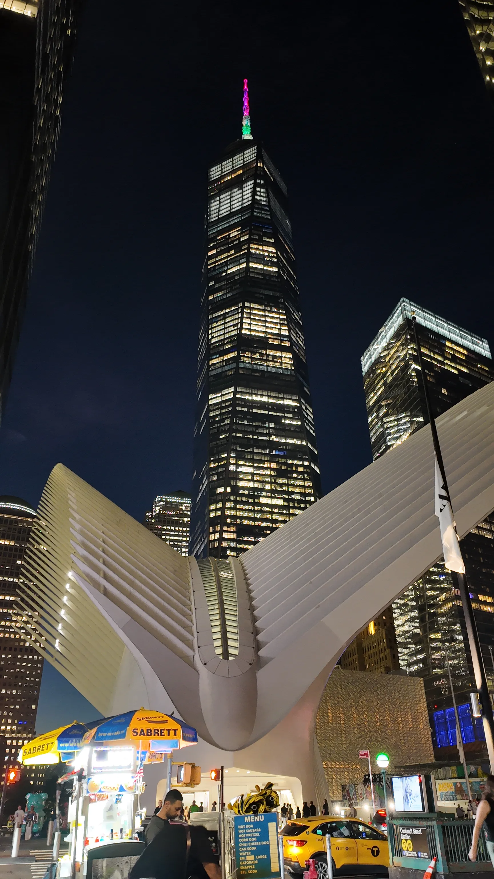 A white ribbed building and illuminated skyscraper at night.