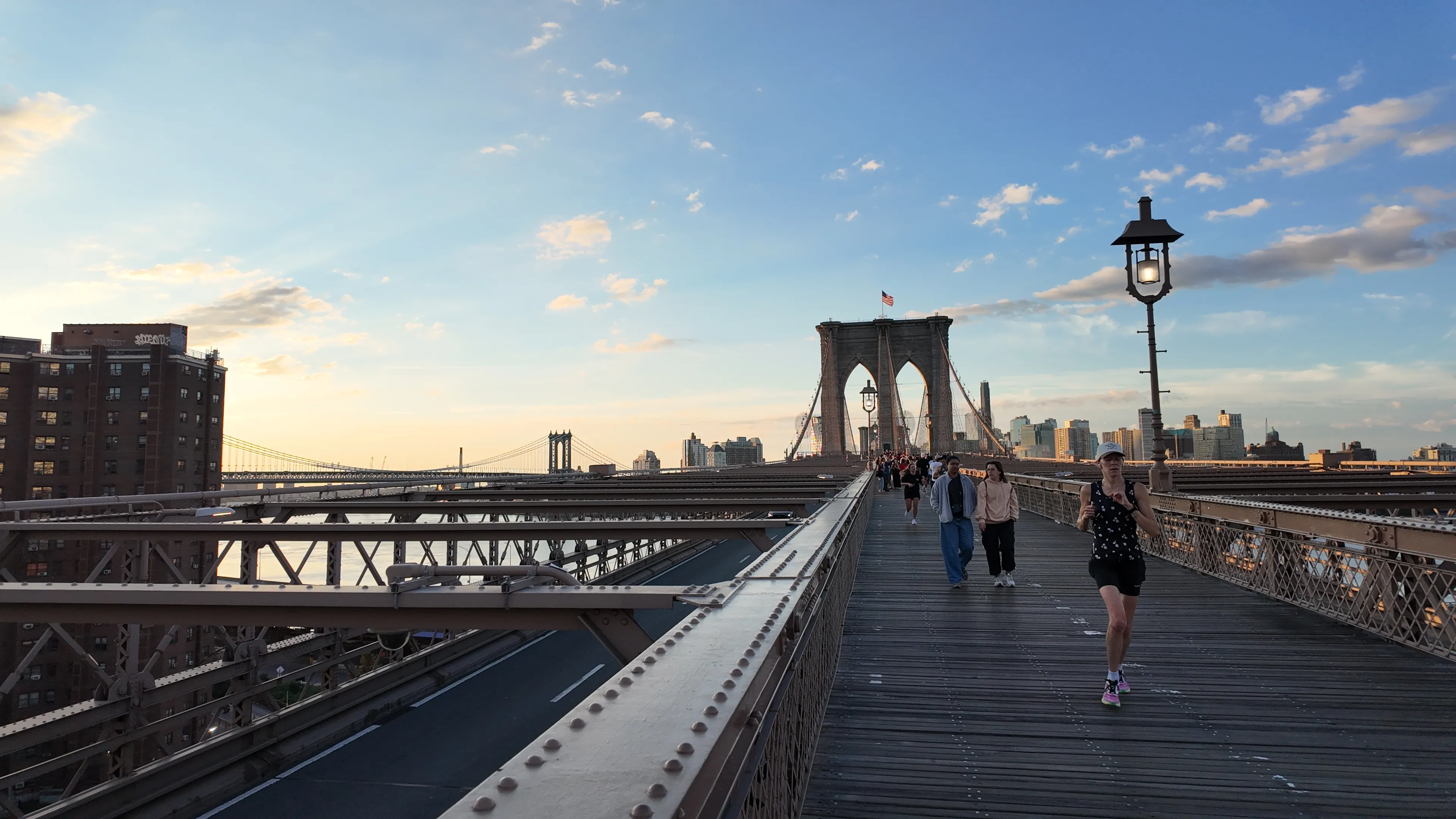 People walking toward a stone bridge tower at sunset.