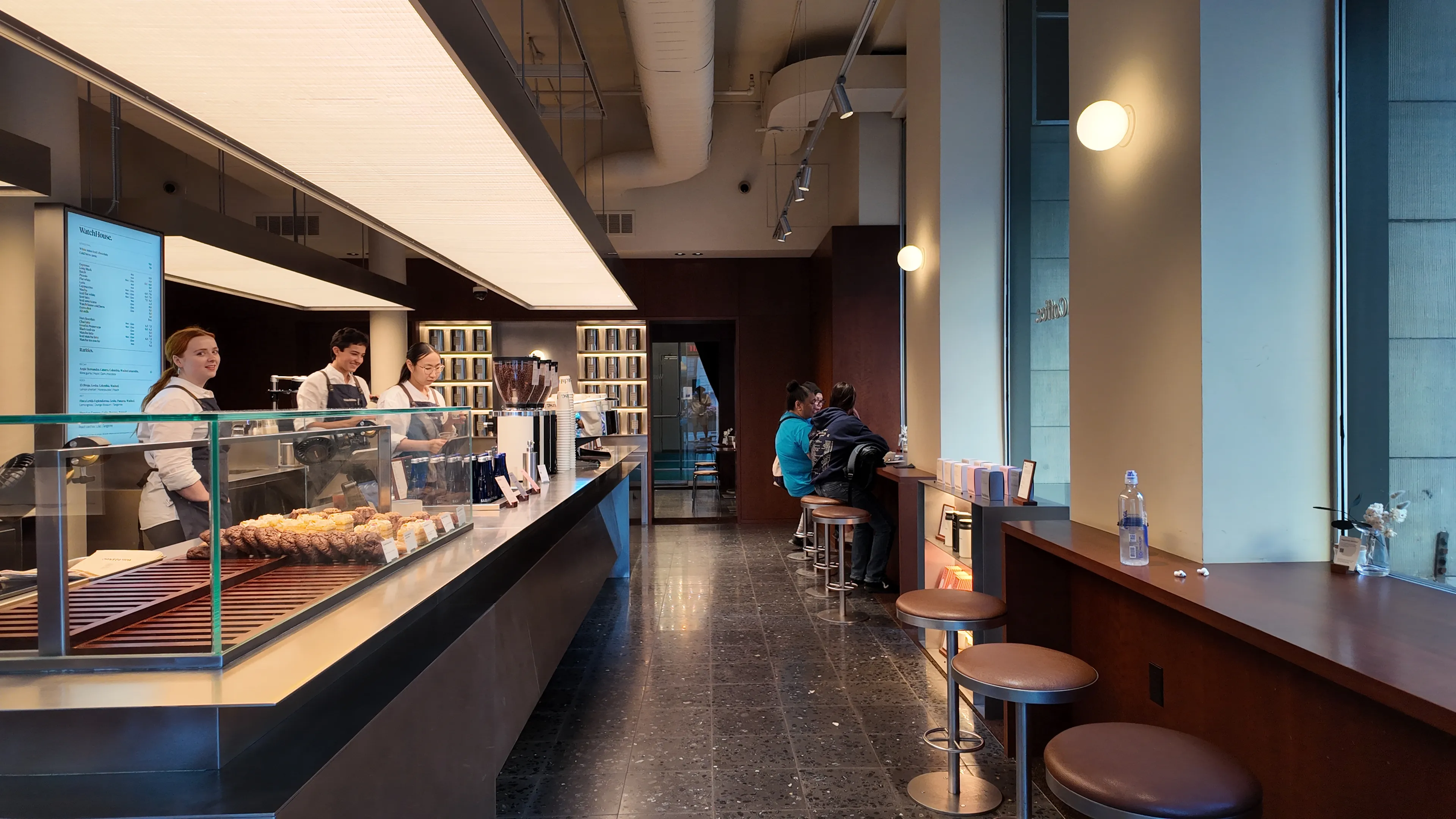 A long cafe counter with pastries and customers.