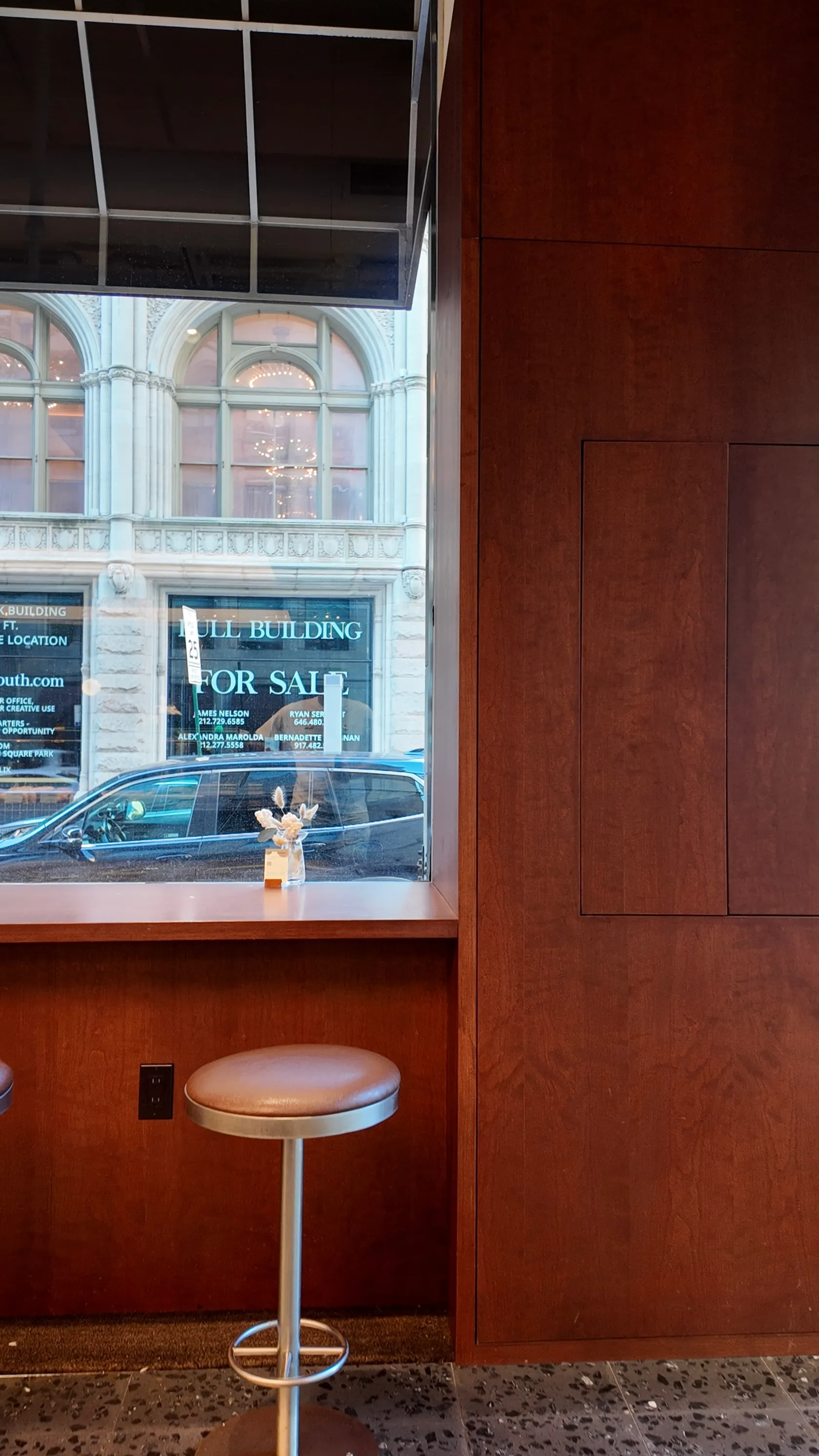 A quiet cafe window and stools against wood-panelled walls.