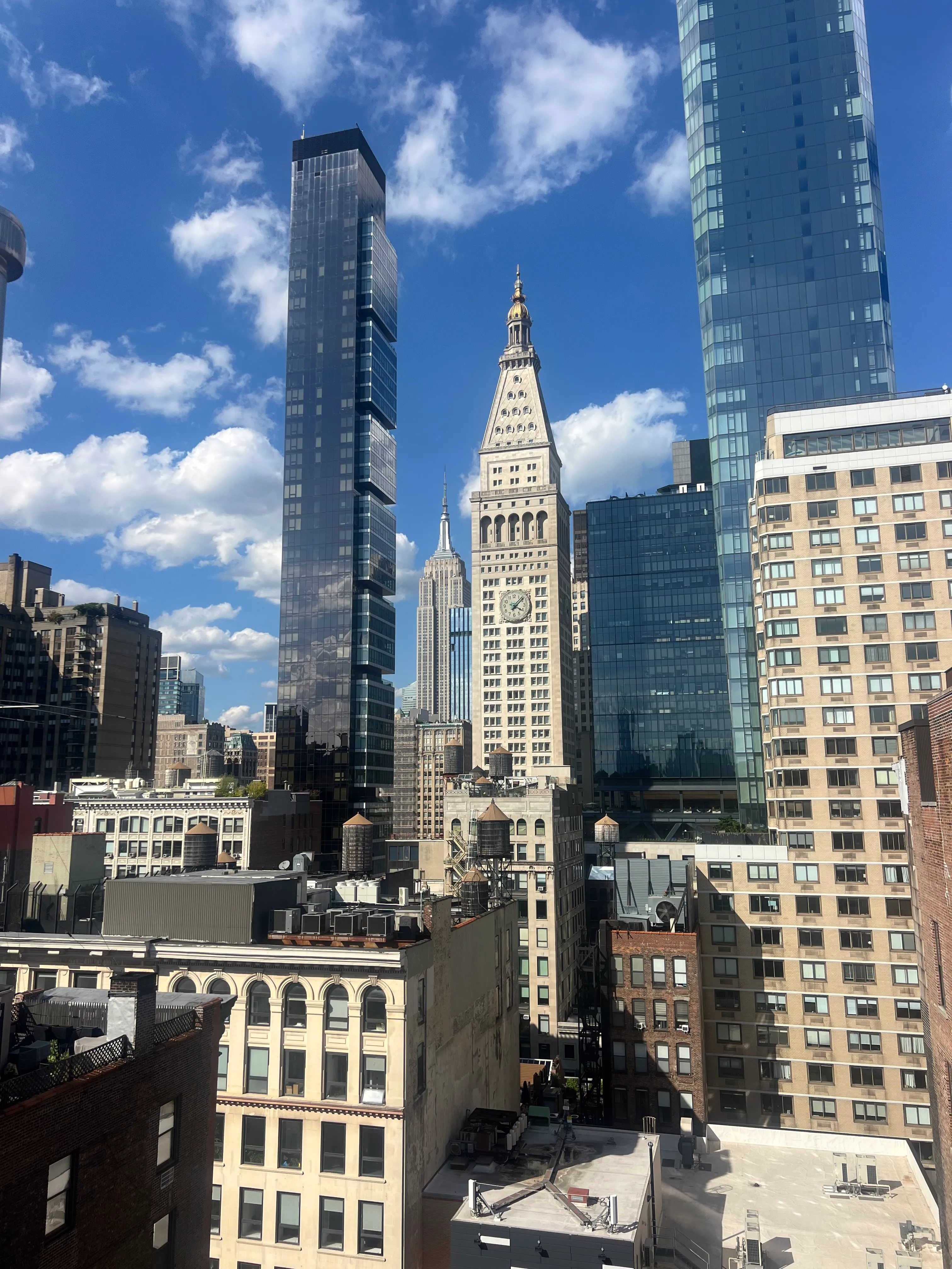 Sunlit skyscrapers and older buildings beneath a blue sky.