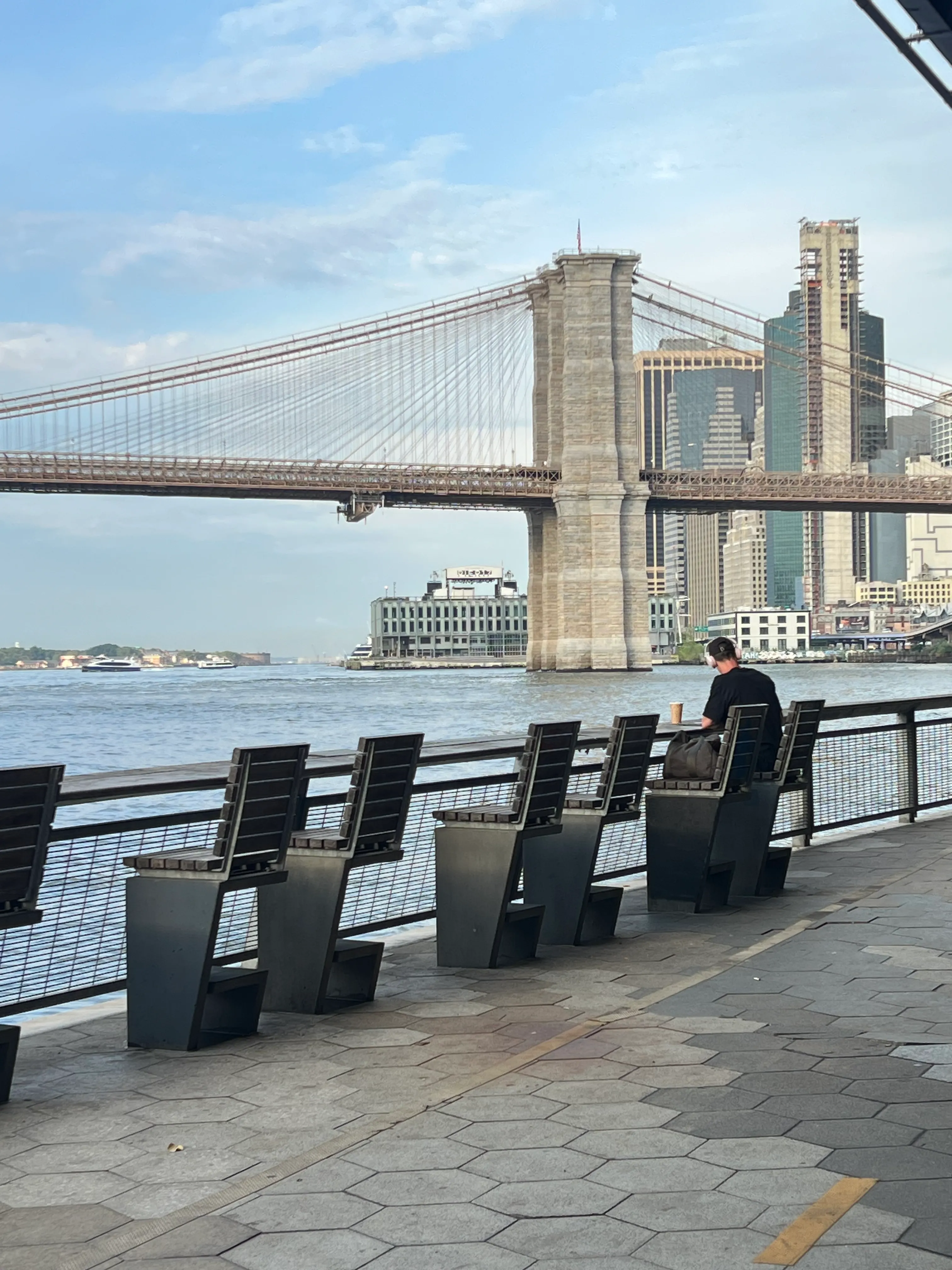 A suspension bridge viewed from a riverside promenade.