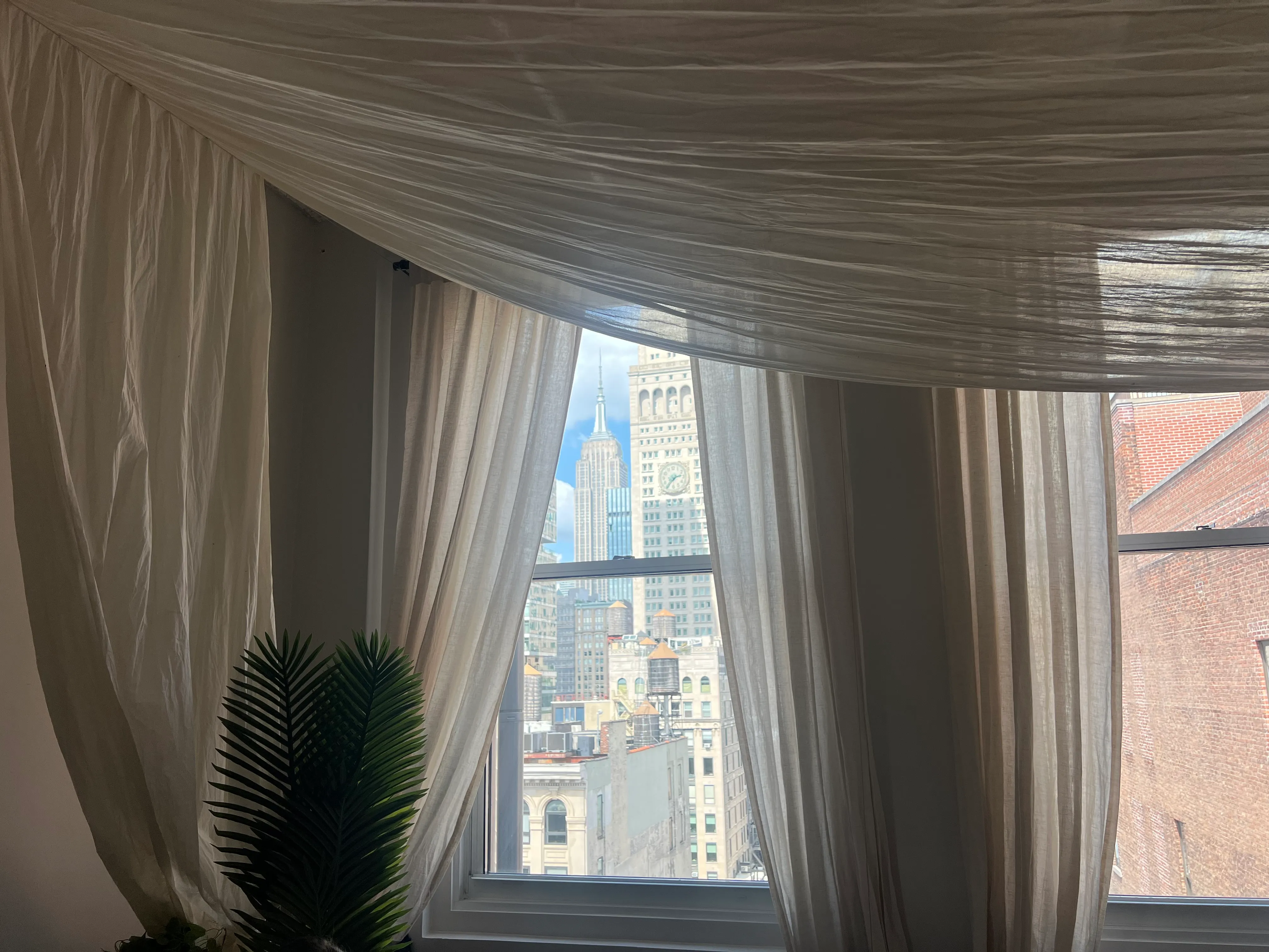 A city view through a window framed by draped fabric.