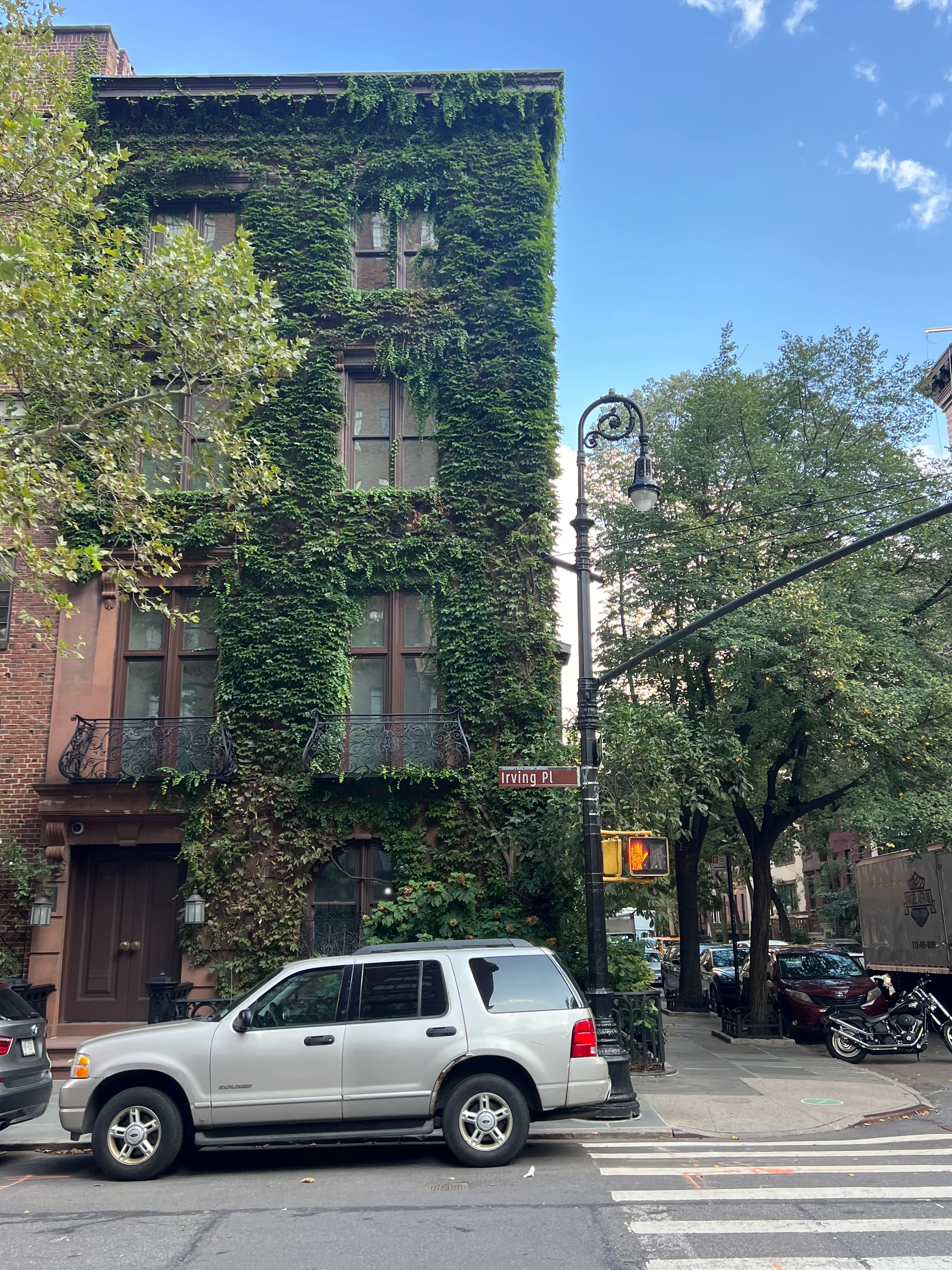 An ivy-covered corner building and trees beside a crosswalk.