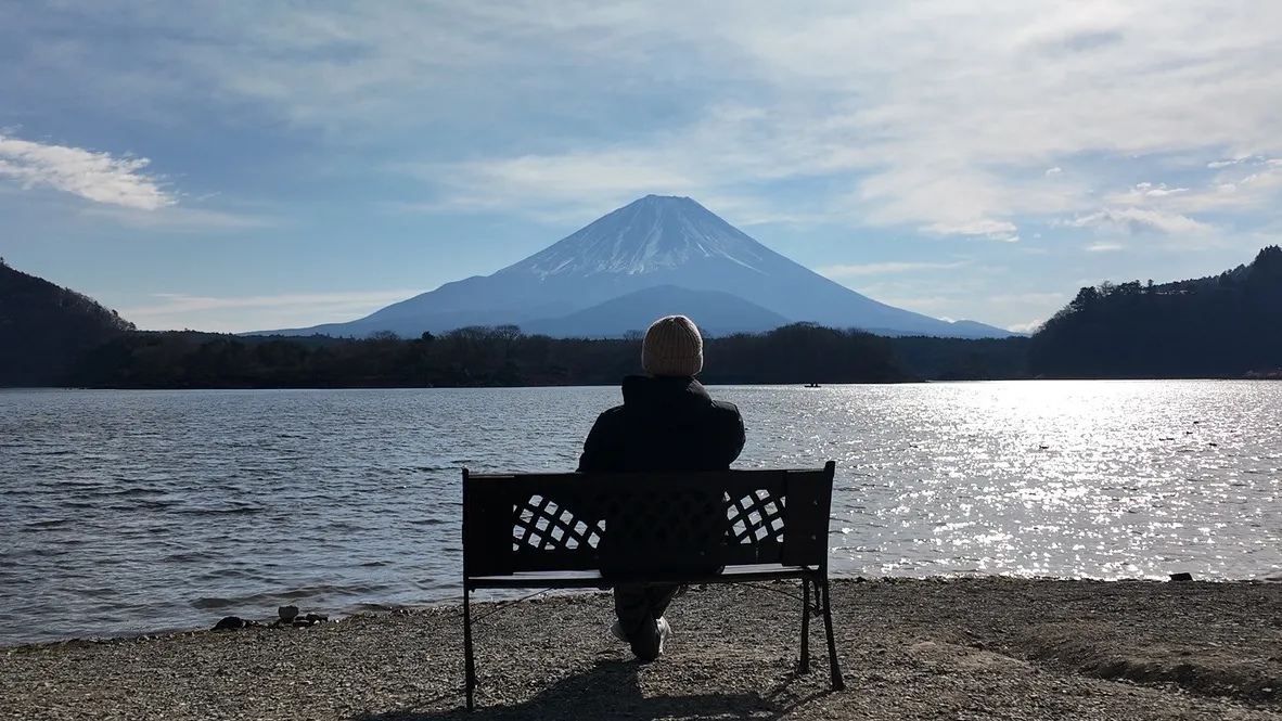 A person seated on a bench facing a lake and mountain.