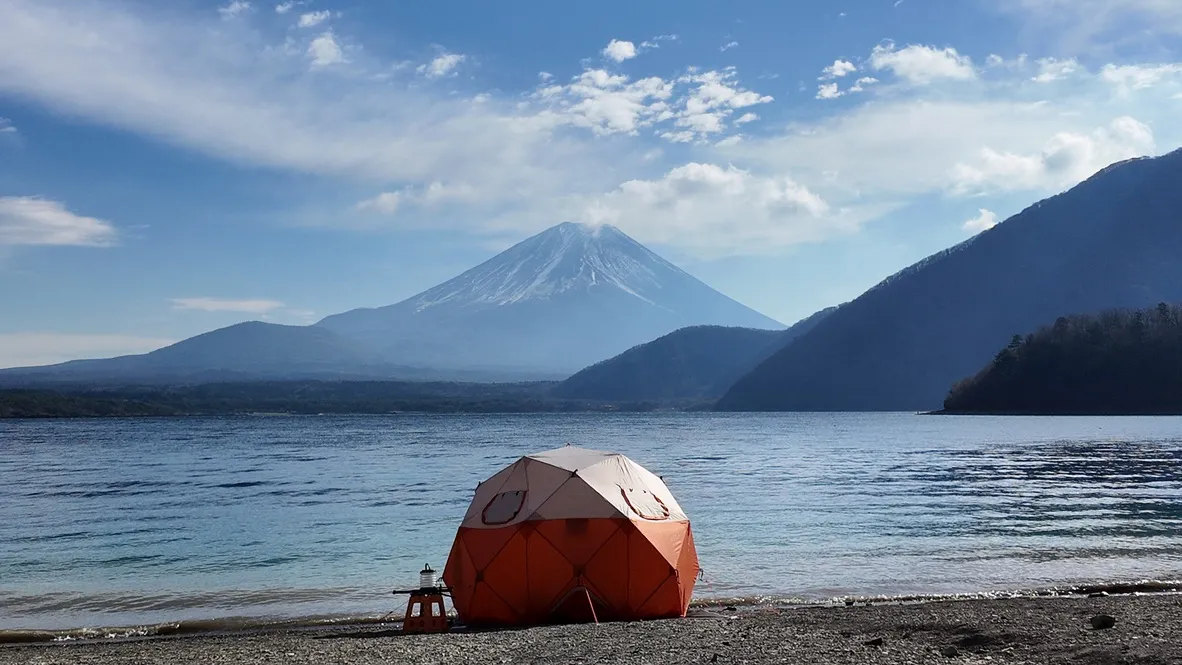 An orange tent on a lakeshore beneath a mountain.