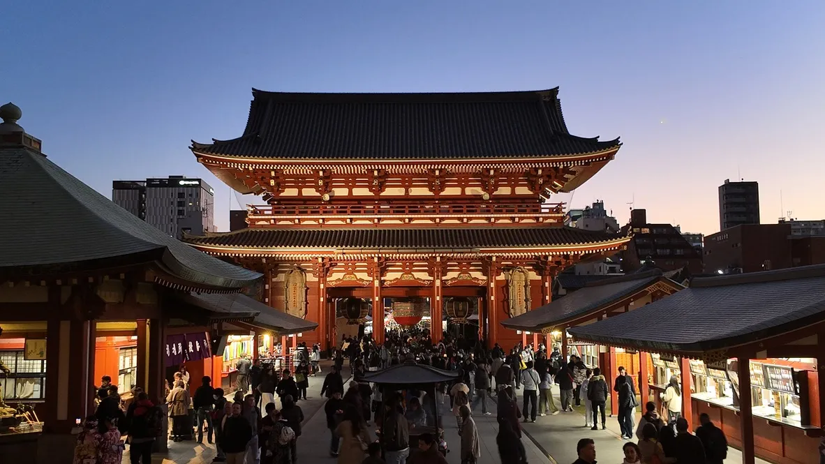 A busy temple courtyard and gate viewed from steps at dusk.