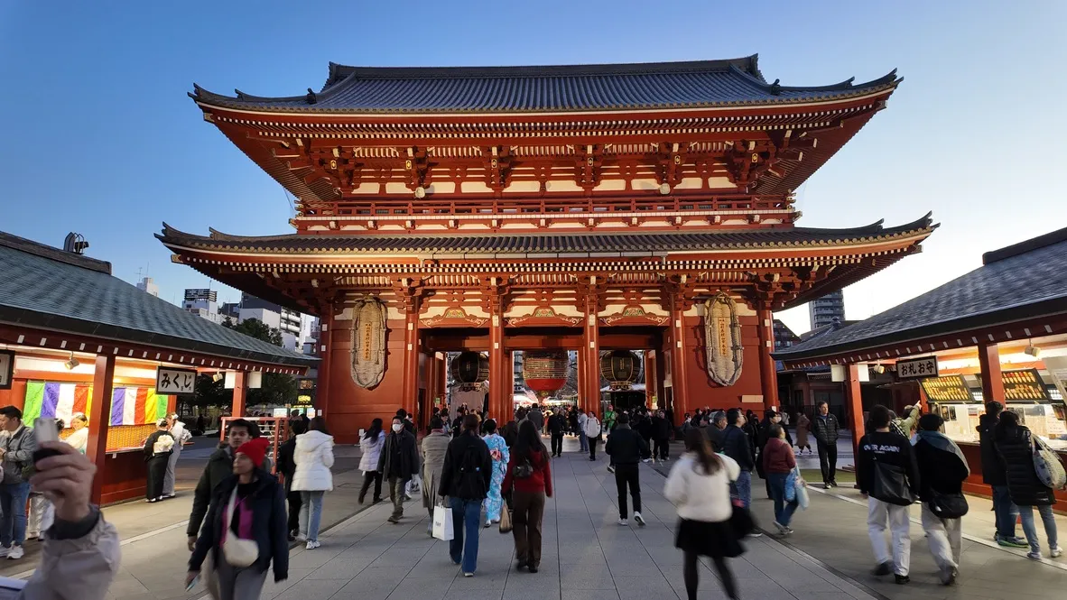 Visitors passing through a large red temple gate.