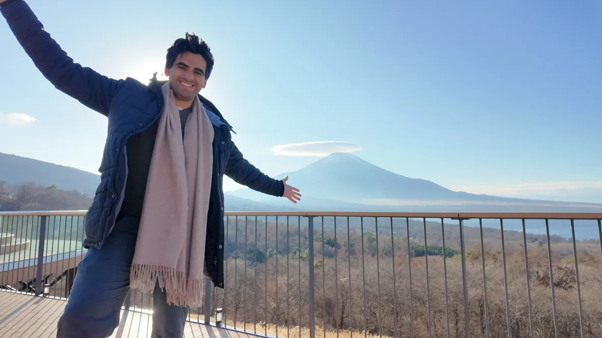 A person posing at a lookout with a mountain in the background.