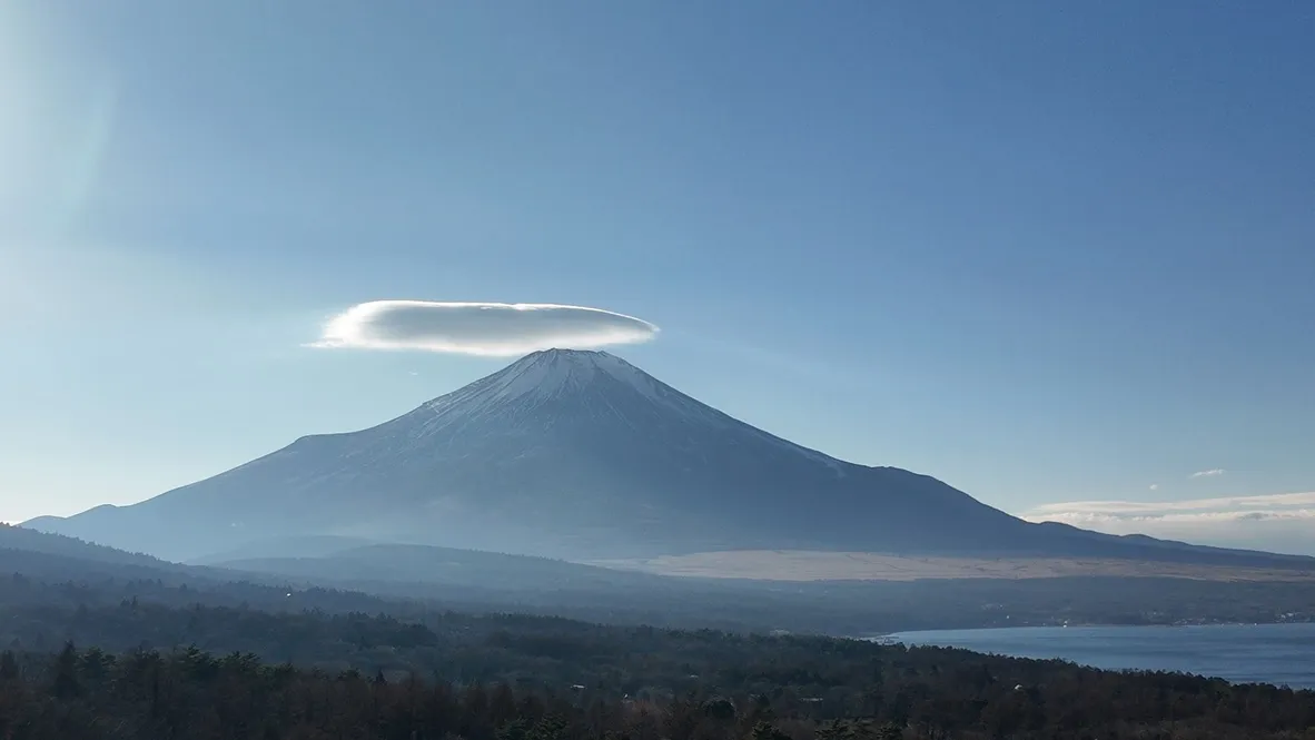A smooth cloud hovering above a mountain summit.