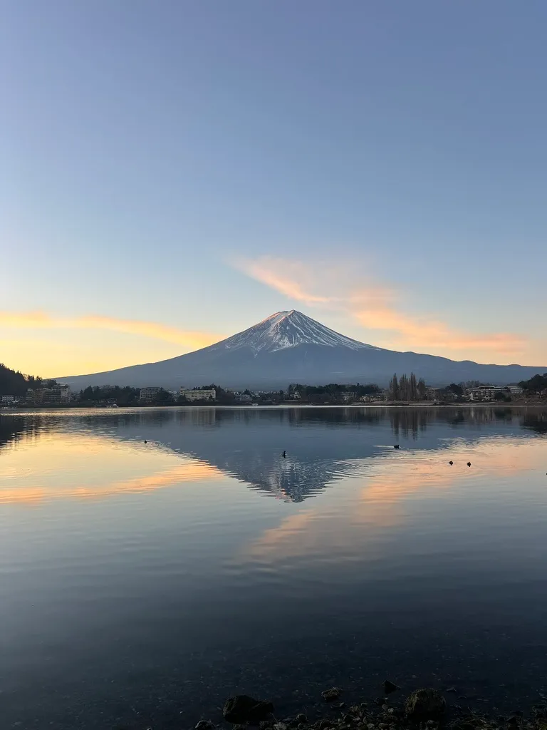 A snow-capped mountain reflected in a lake beneath a pastel dawn sky.