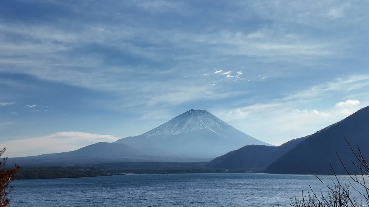 A snow-capped mountain beyond a lake and wooded hills.