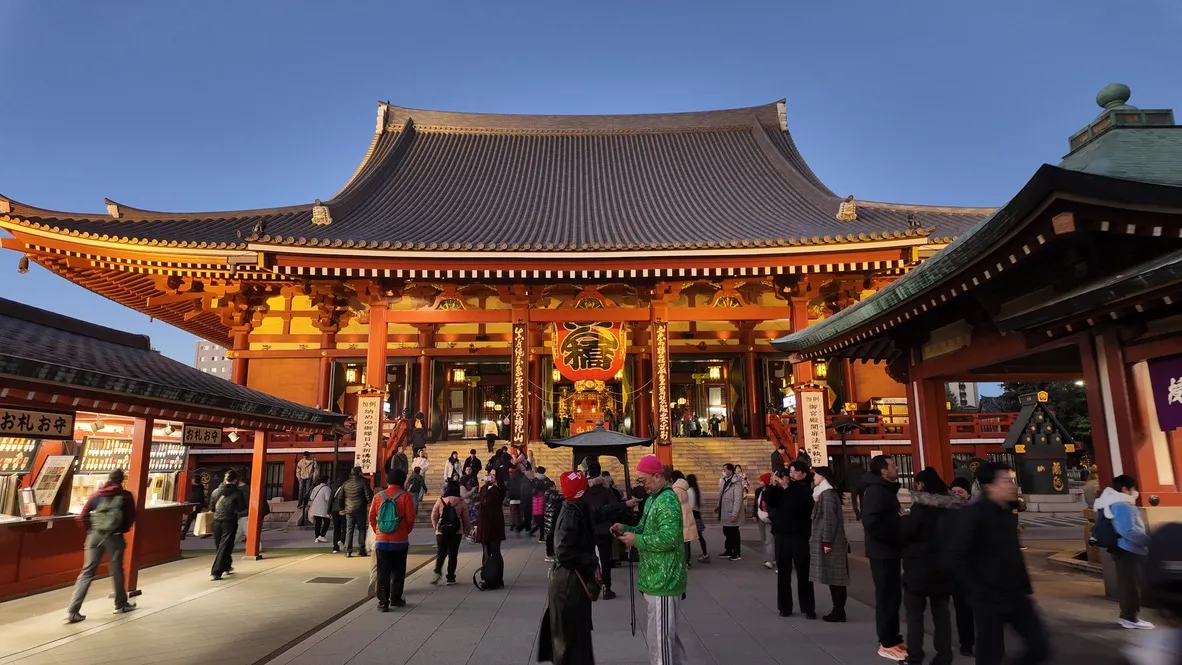 Visitors outside an illuminated red temple hall.