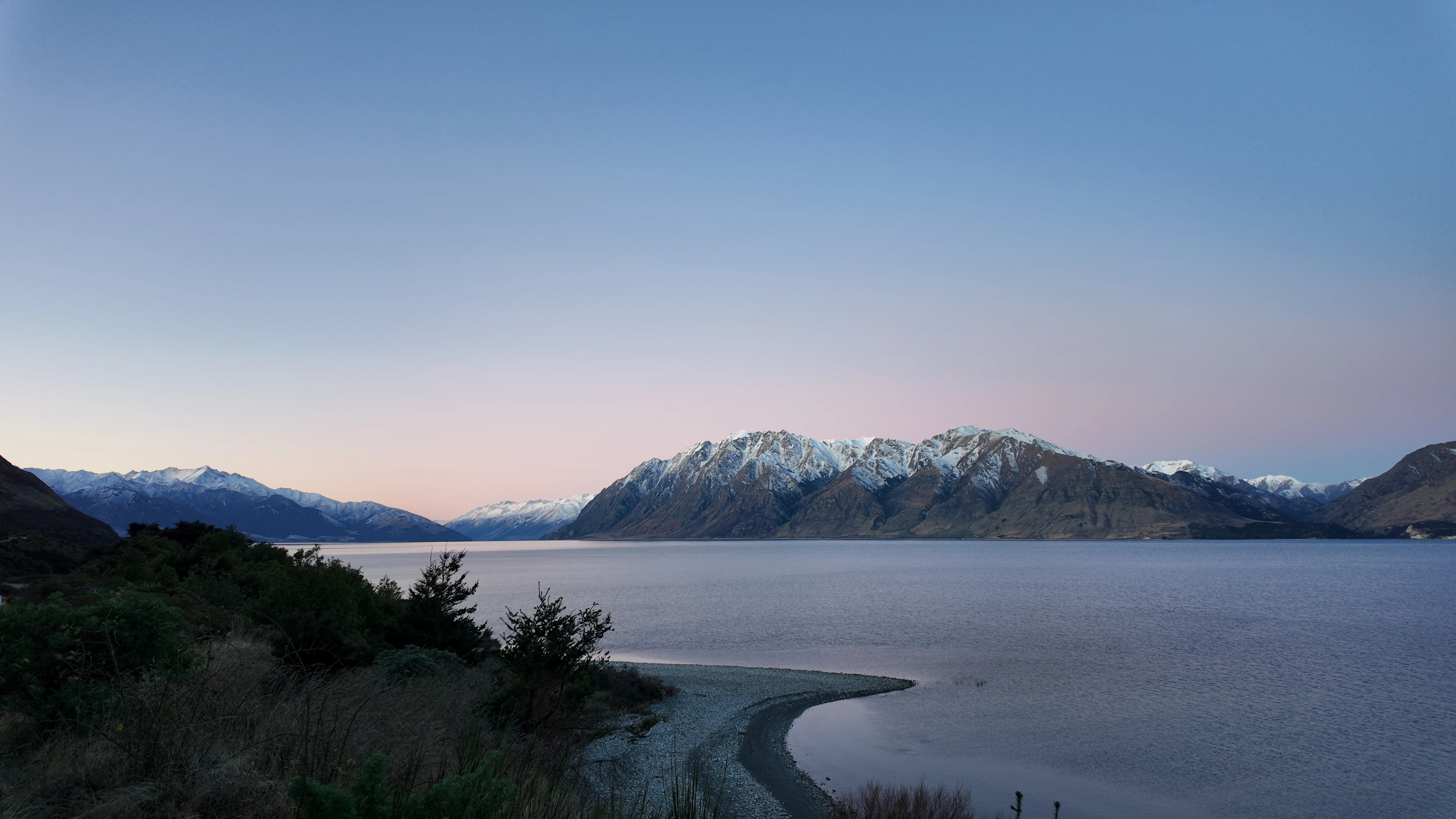 A lakeside beach and snow-capped mountains at dusk.