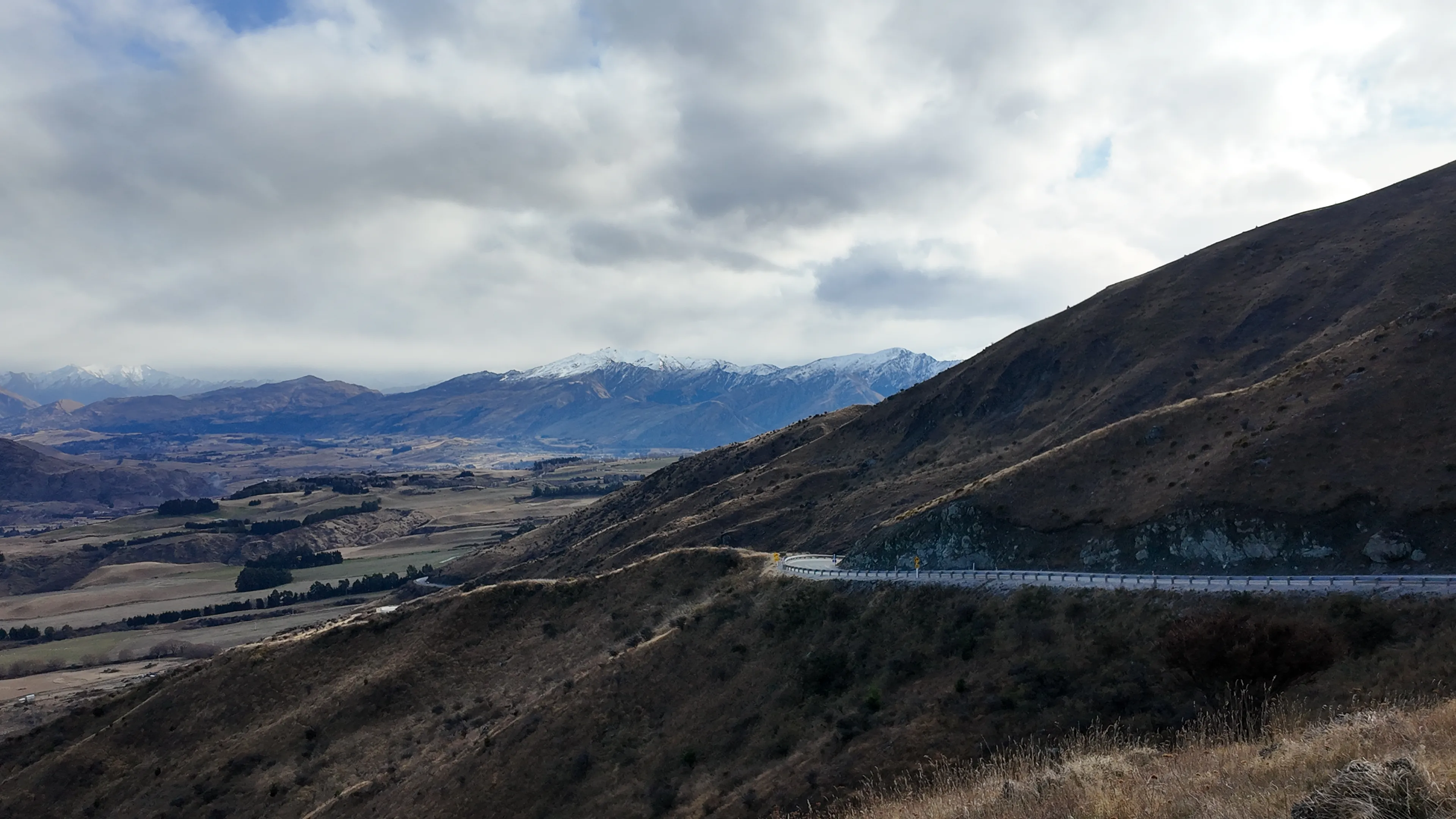 A winding mountain road above a broad valley beneath a cloudy sky.