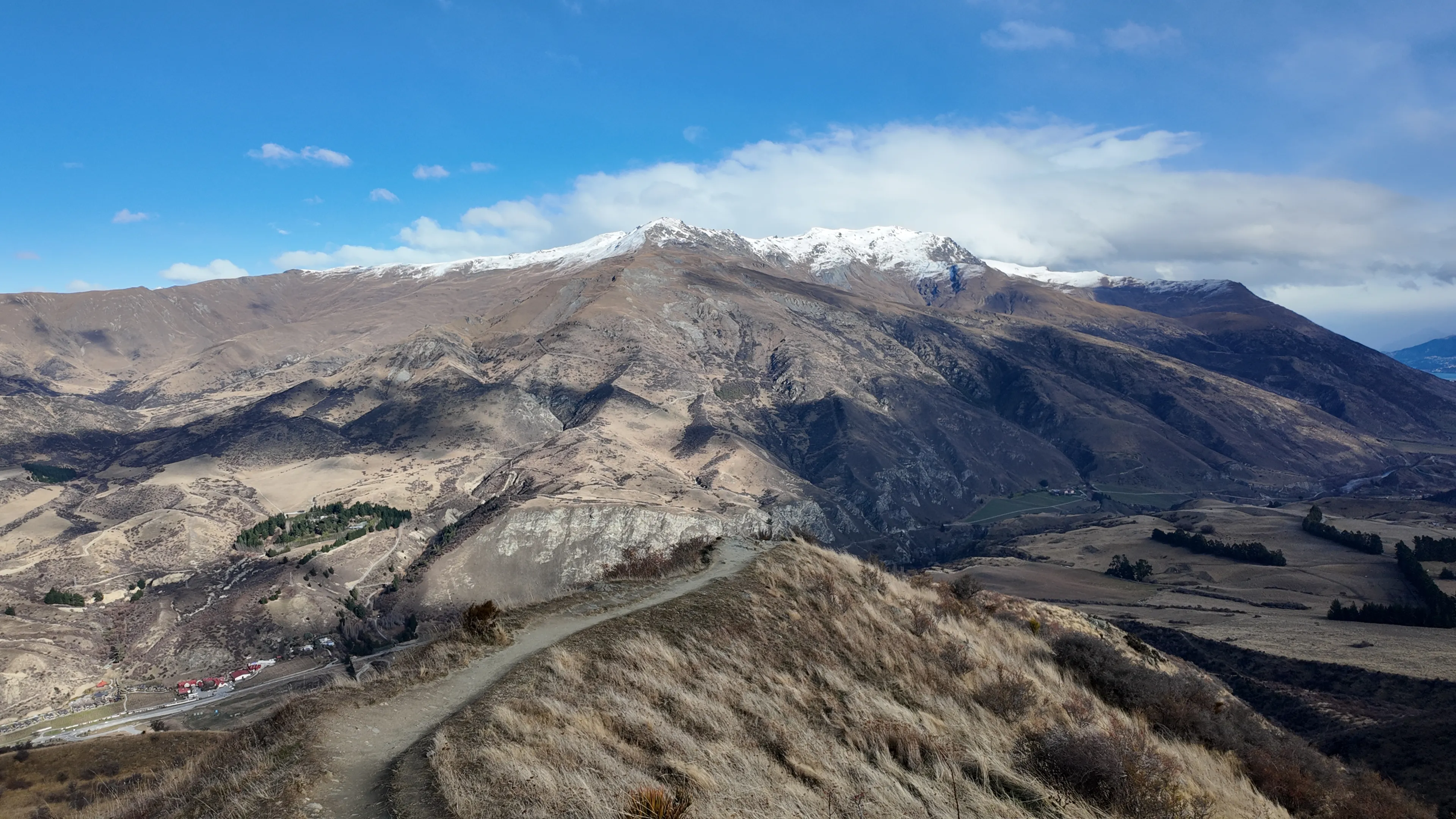 A hillside trail overlooking a valley and snow-dusted mountain peaks.