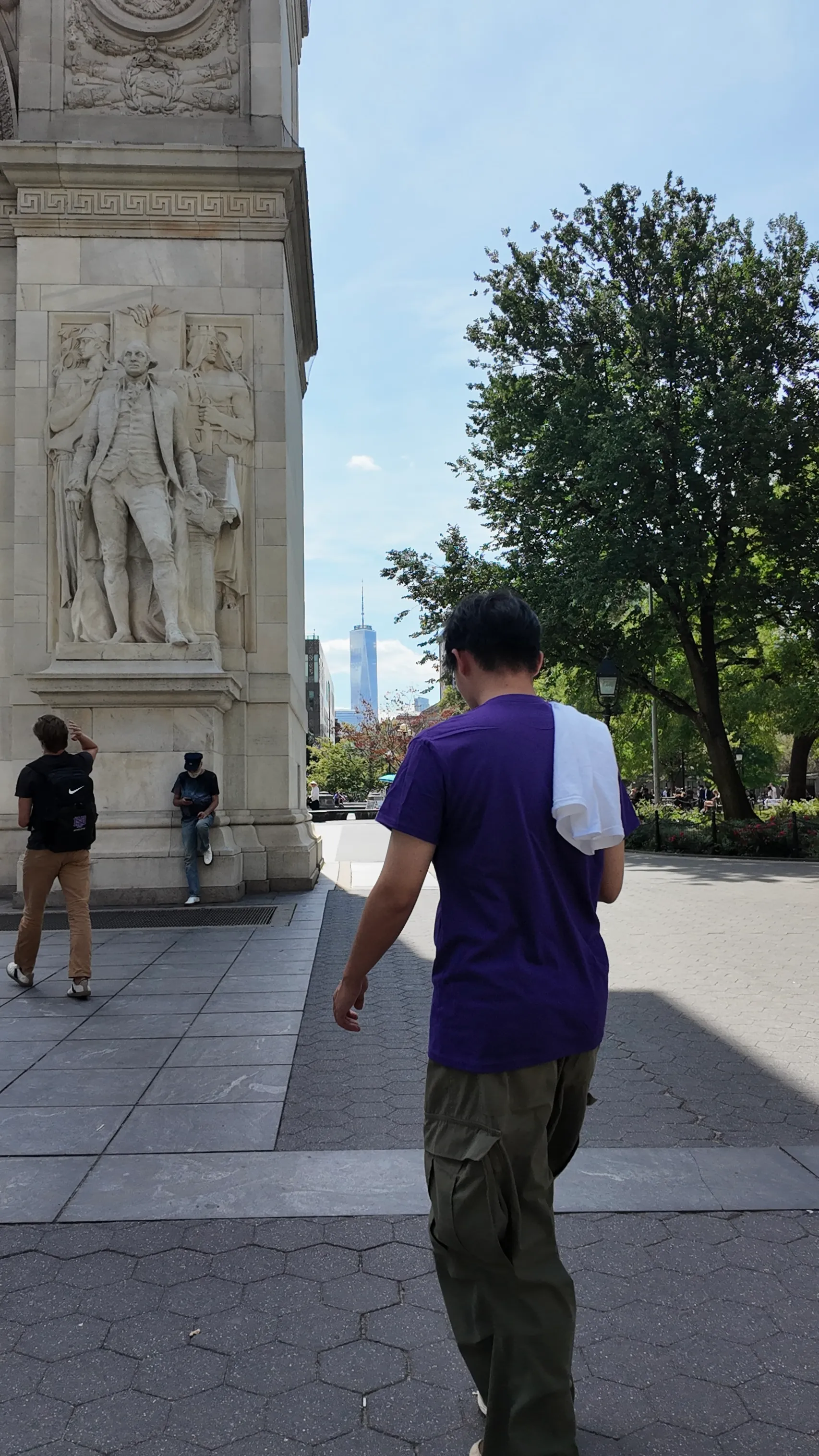 A person walking beside a stone arch in a leafy New York park.
