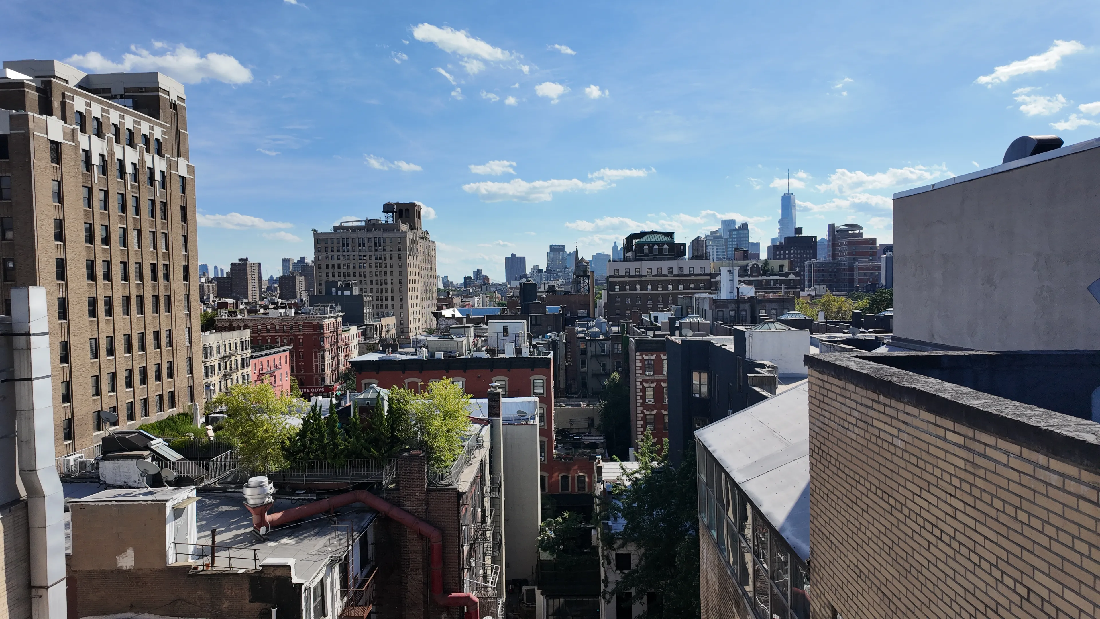 A view over New York rooftops, water towers and terraces beneath a blue sky.