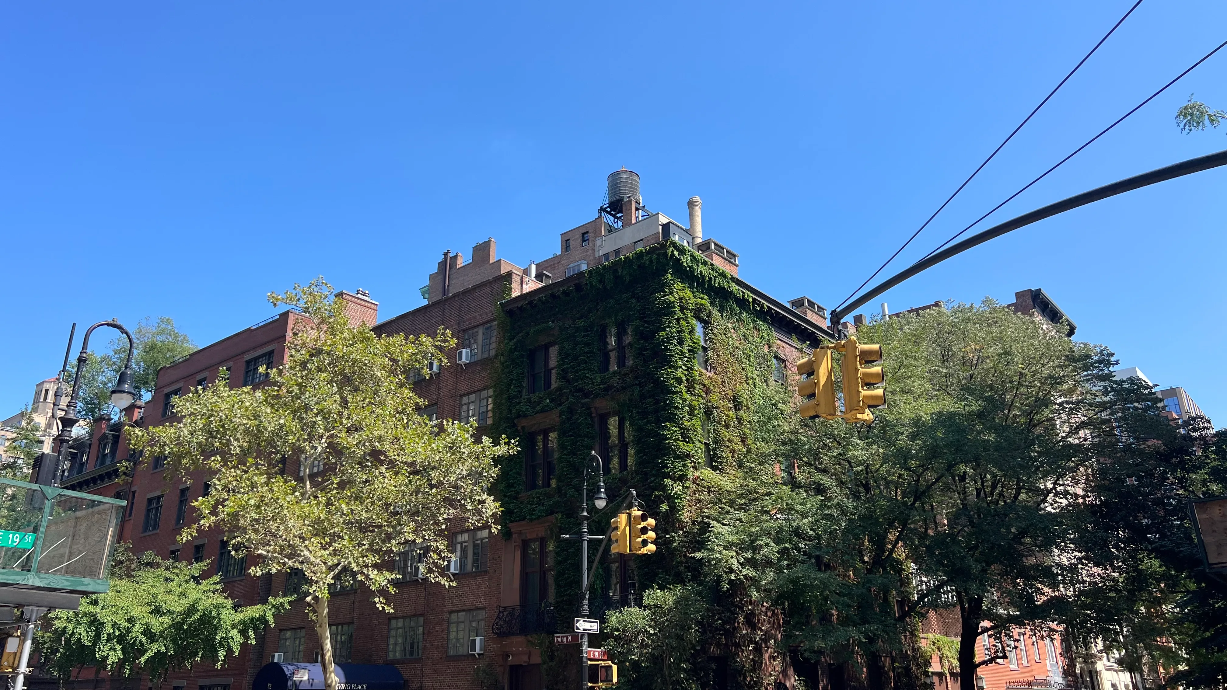 An ivy-covered brick building and traffic lights on a sunny New York street.